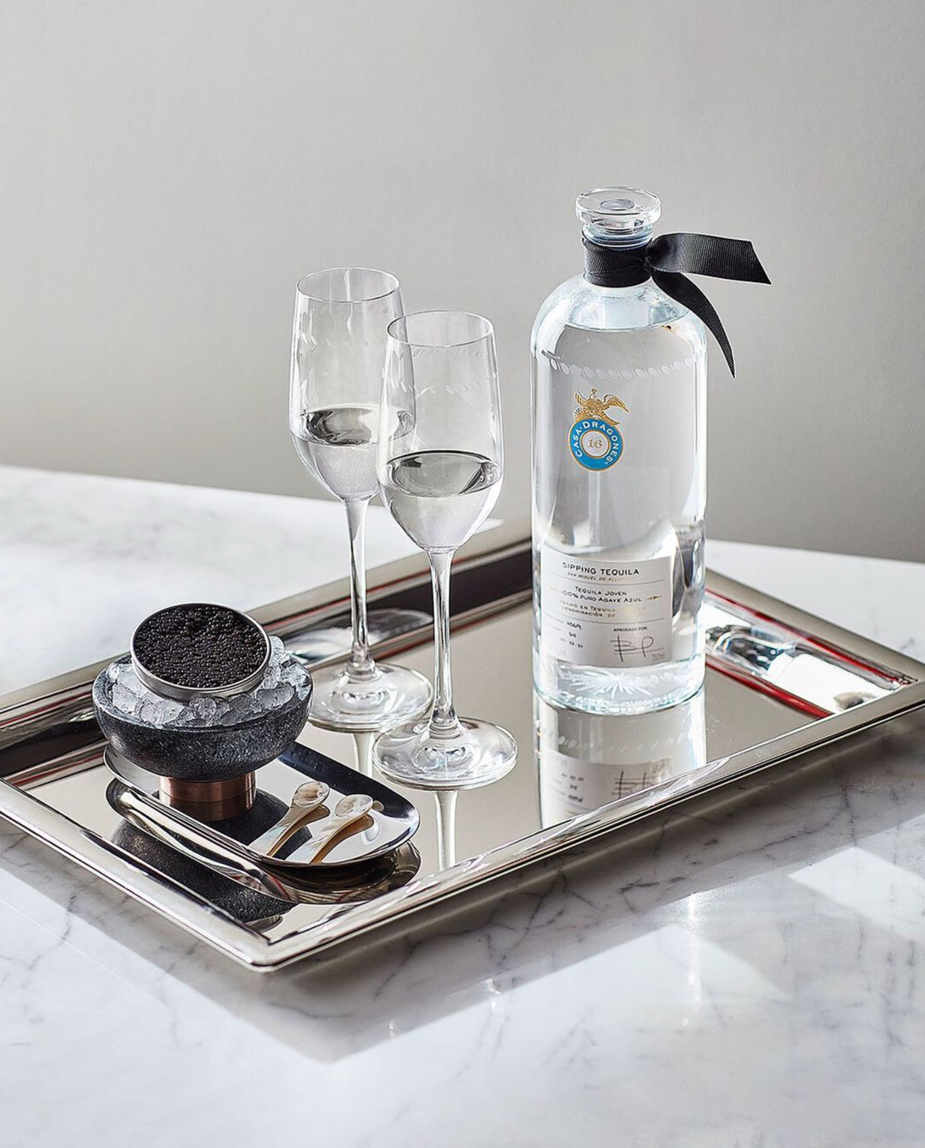 Casa Dragones Joven Tequila gift set featuring a bottle and glass flutes on a silver tray.