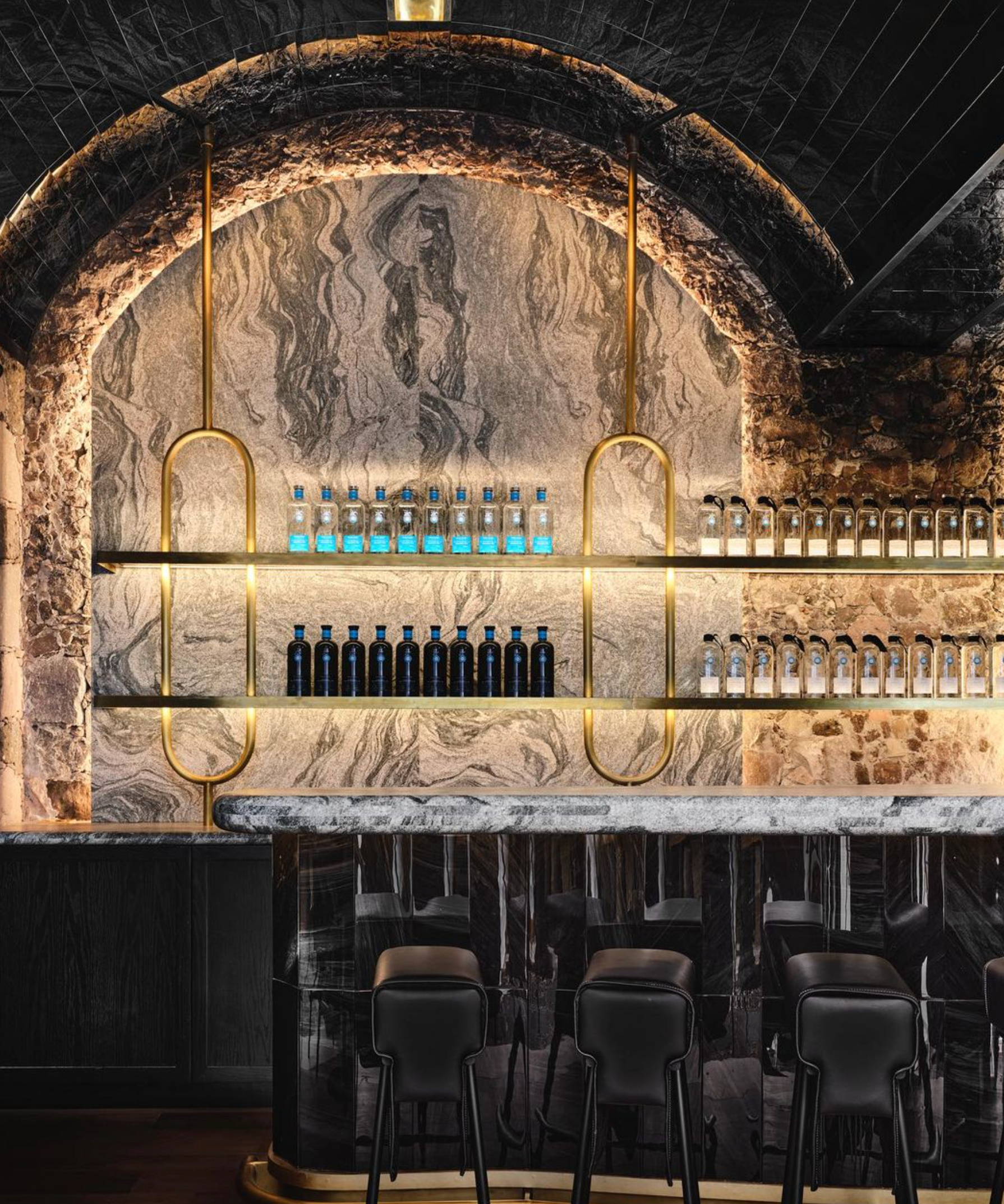 Stylish bar interior with marble walls, glowing shelves of tequila bottles, and elegant black chairs.
