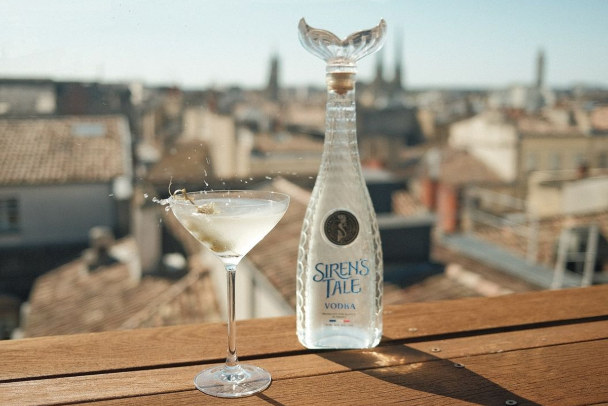 Siren's Tale French Vodka bottle beside a martini glass with a splash, showcasing refined elegance in a rooftop setting.