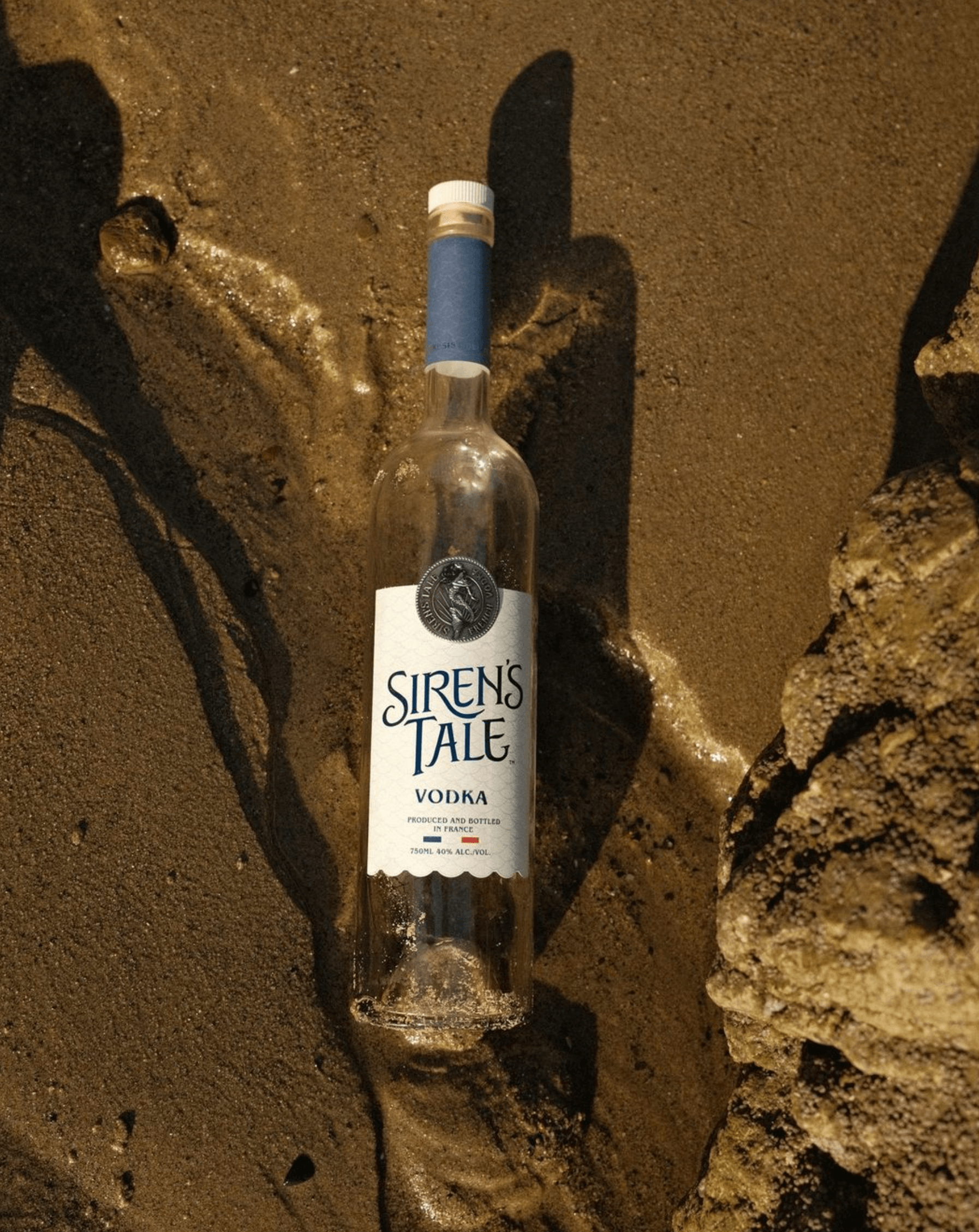 Siren's Tale vodka bottle on a sandy beach, showcasing its elegant design and craftsmanship.