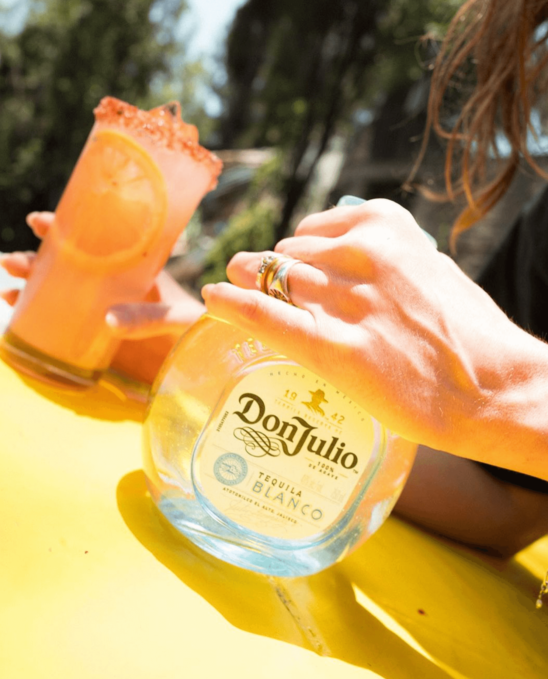 Don Julio Blanco Tequila bottle held with a refreshing cocktail, showcasing its crisp agave flavor in a vibrant setting.