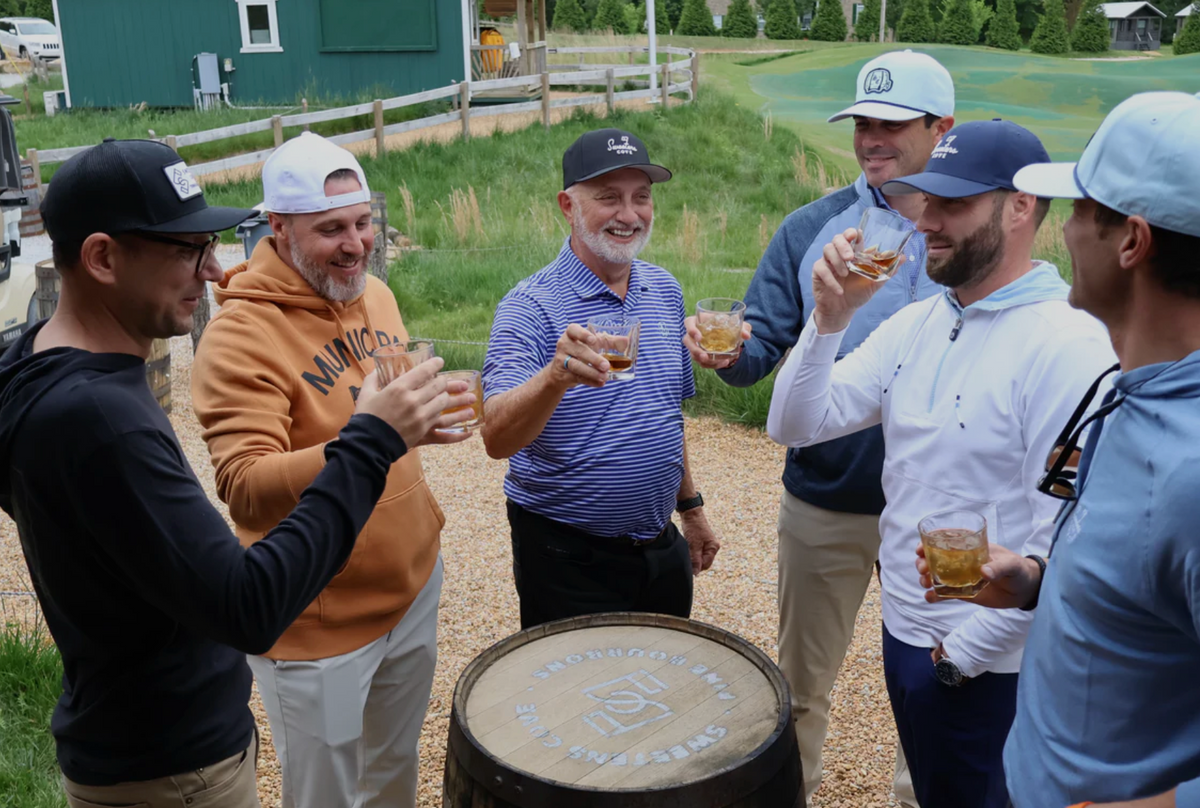 Group of friends enjoying Sweetens Cove Tennessee Bourbon outside, celebrating with glasses raised on a sunny day.