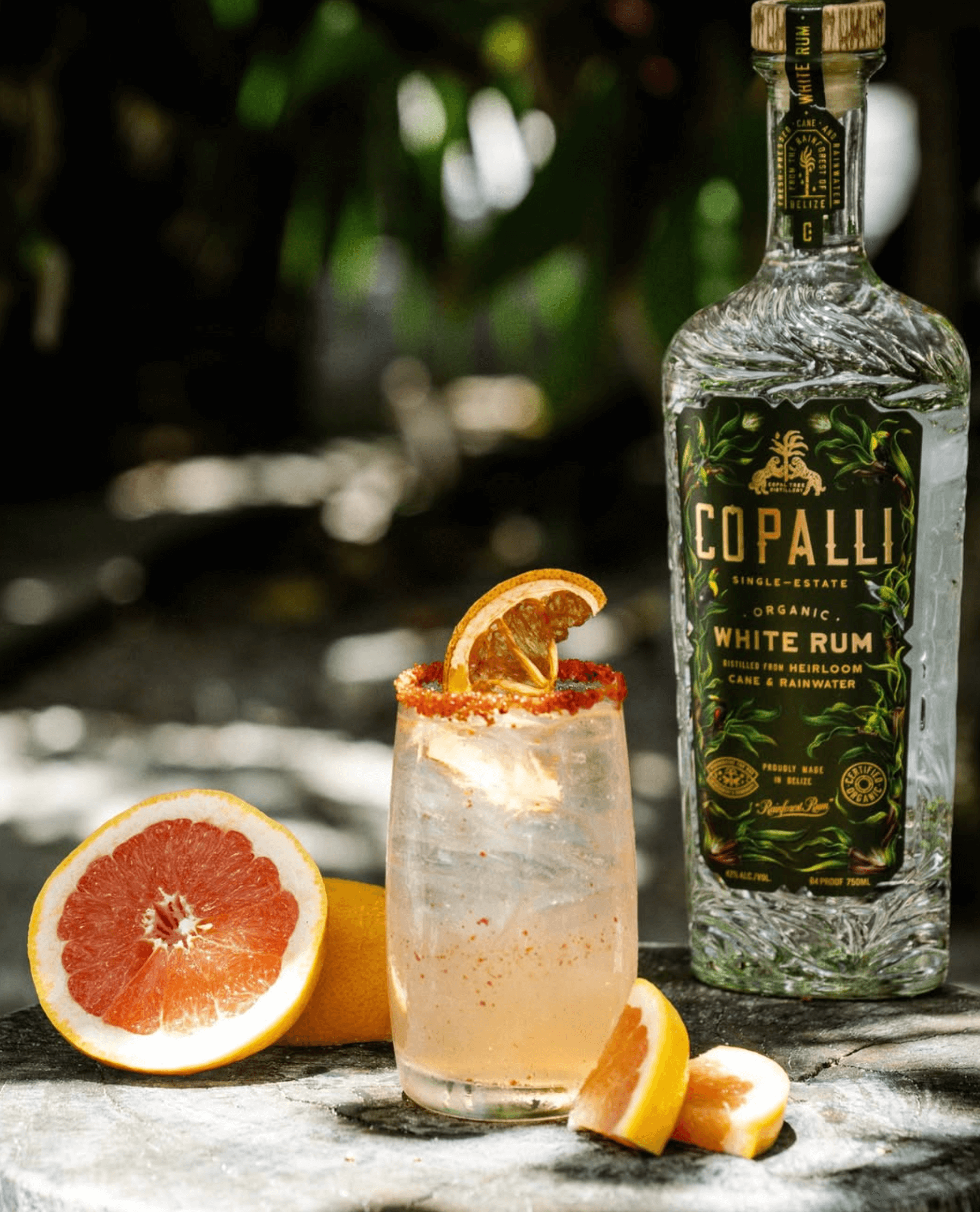 Copalli White Belizean Rum cocktail garnished with citrus on a rustic table in a tropical setting.