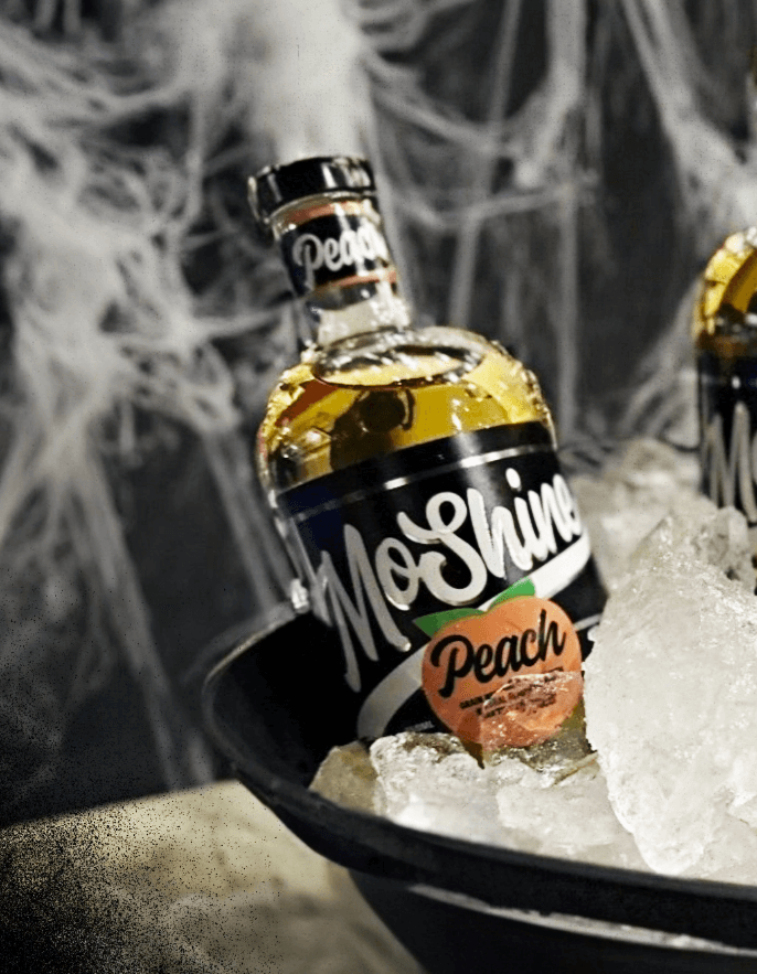 MoShine Peach Moonshine bottle on ice, featuring Southern peach flavor and velvety smooth finish.