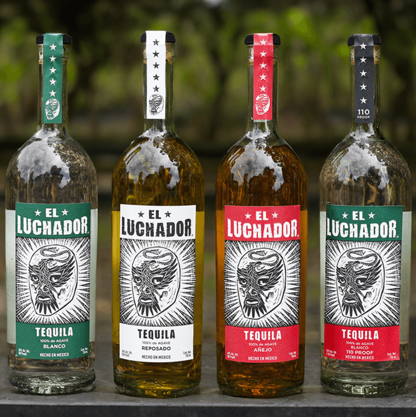 Four bottles of El Luchador Tequila: Blanco, Reposado, Añejo, and 110 Proof displayed outdoors.