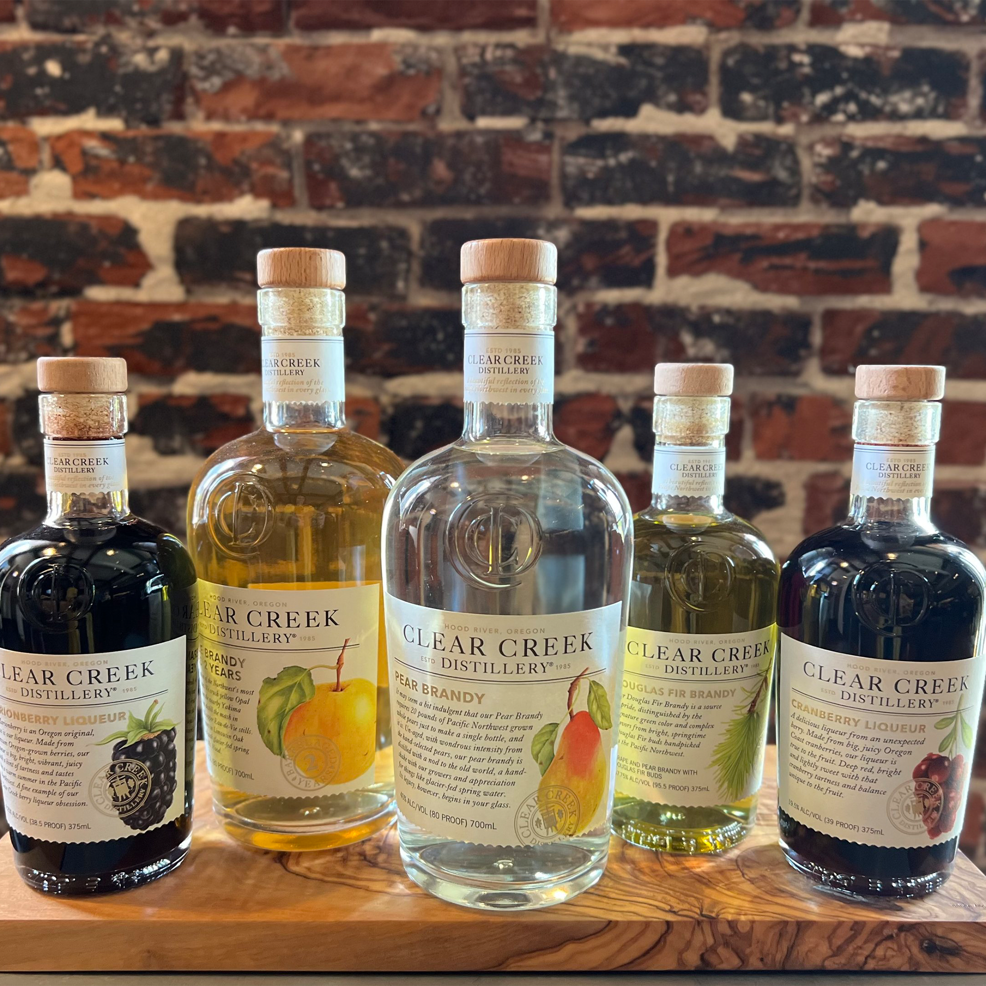 Collection of Clear Creek Distillery fruit brandies including Douglas Fir, Pear, and more on a rustic wooden surface.