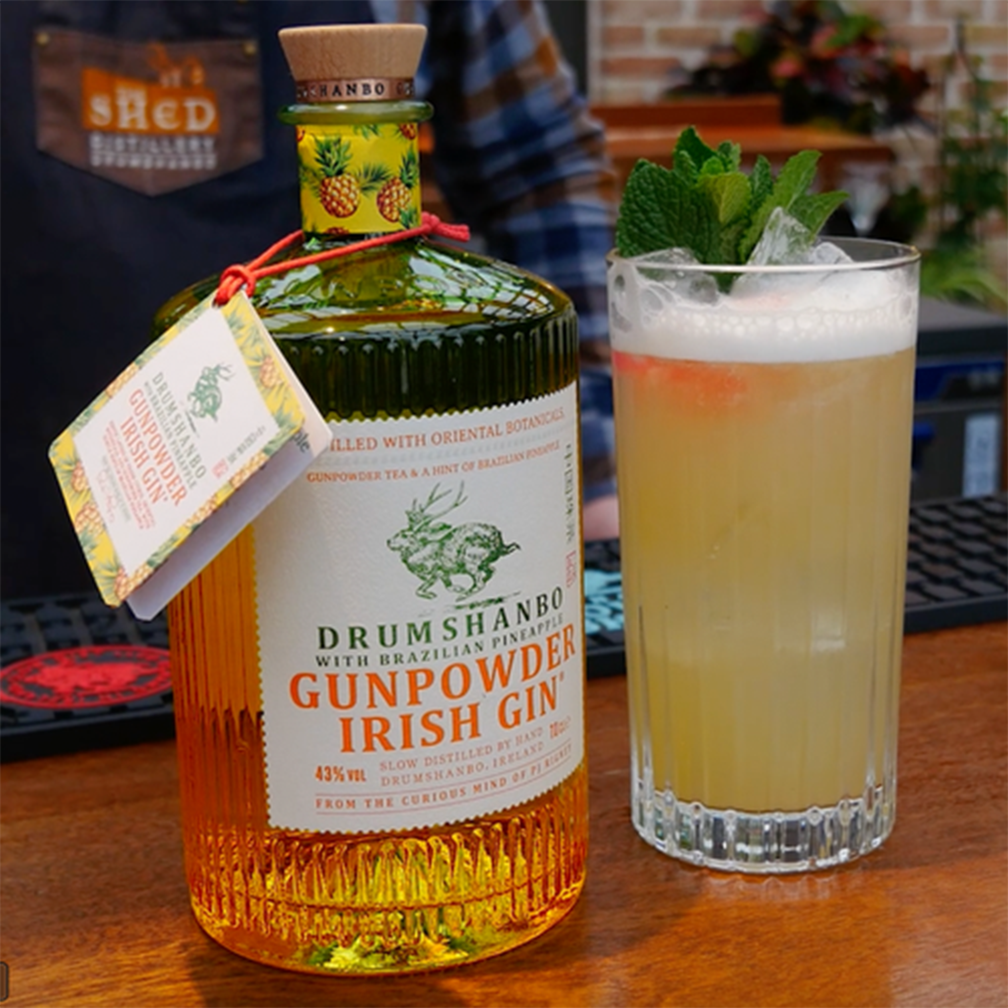 Bottle of Drumshanbo Brazilian Pineapple Gunpowder Irish Gin next to a refreshing cocktail garnished with mint.