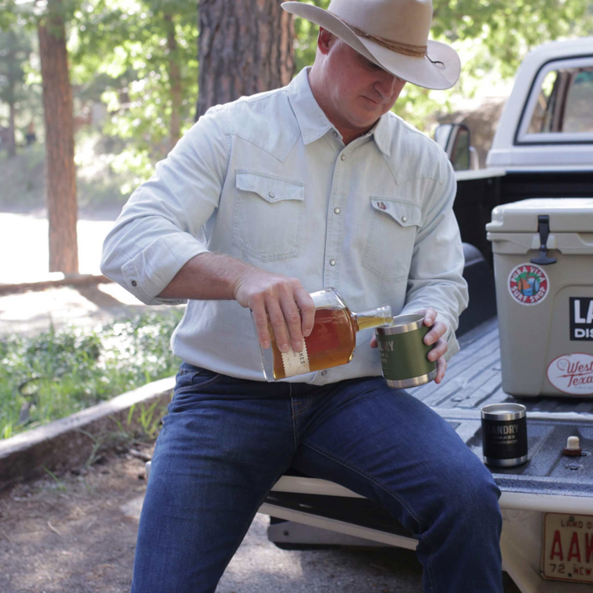 Man pouring Landry Stakes Small Batch Bourbon Whiskey into a glass at a rustic outdoor setting.
