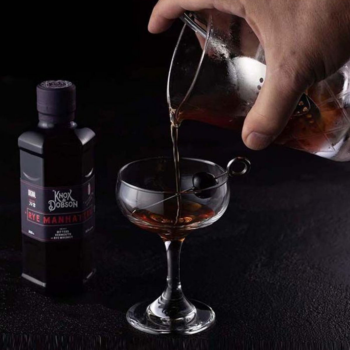 Pouring Knox & Dobson Rye Manhattan cocktail into a glass, showcasing the high-quality handcrafted drink.