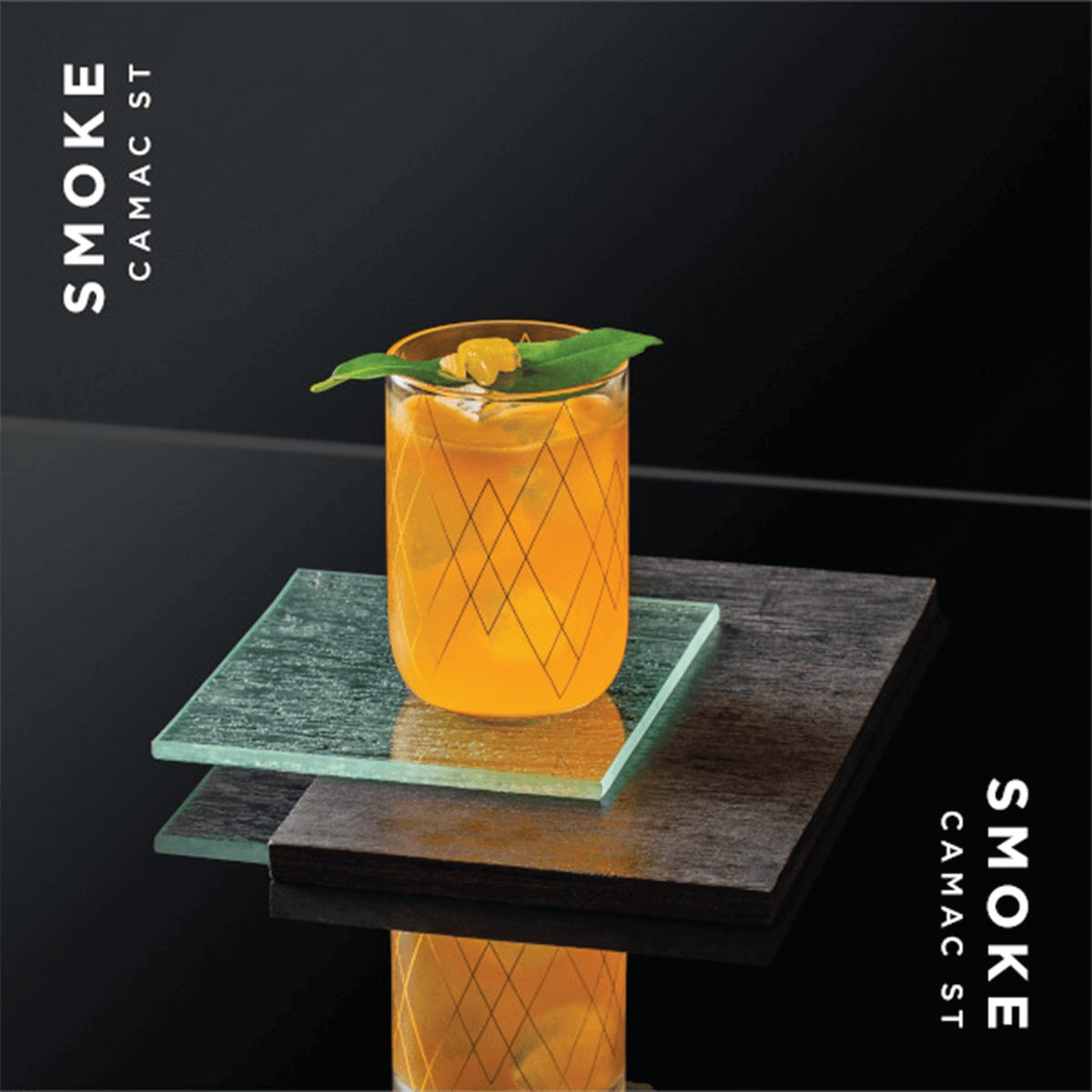 Vibrant orange cocktail served in a patterned glass, featuring fresh herbs, on a stylish black and green background.
