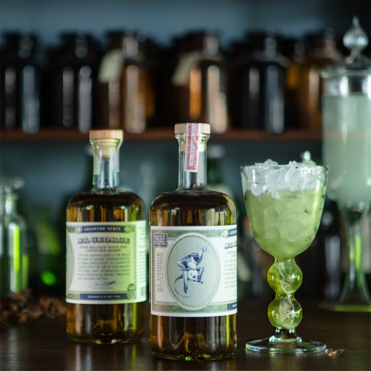 St. George Absinthe Verte 200ml bottles with a green cocktail on a wooden shelf surrounded by various glass jars.