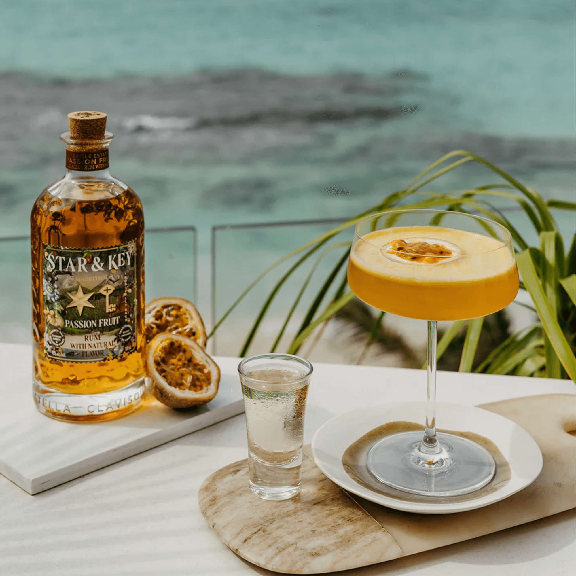 Star & Key Passionfruit Rum bottle with a vibrant Passionfruit Martini and shot glass on a tropical beach backdrop.