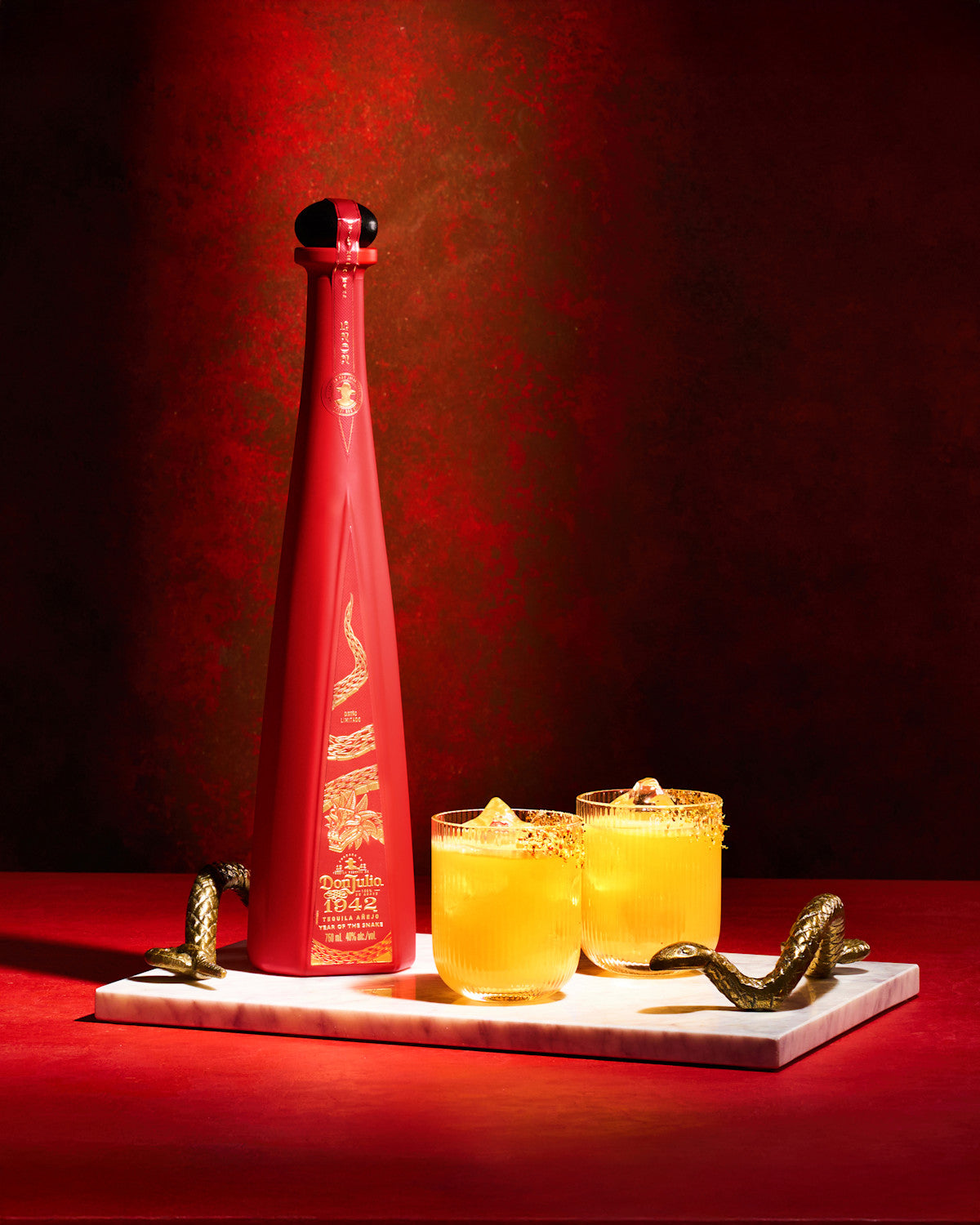 Don Julio 1942 Year of the Snake tequila bottle with cocktails and gold accents on a marble tray.