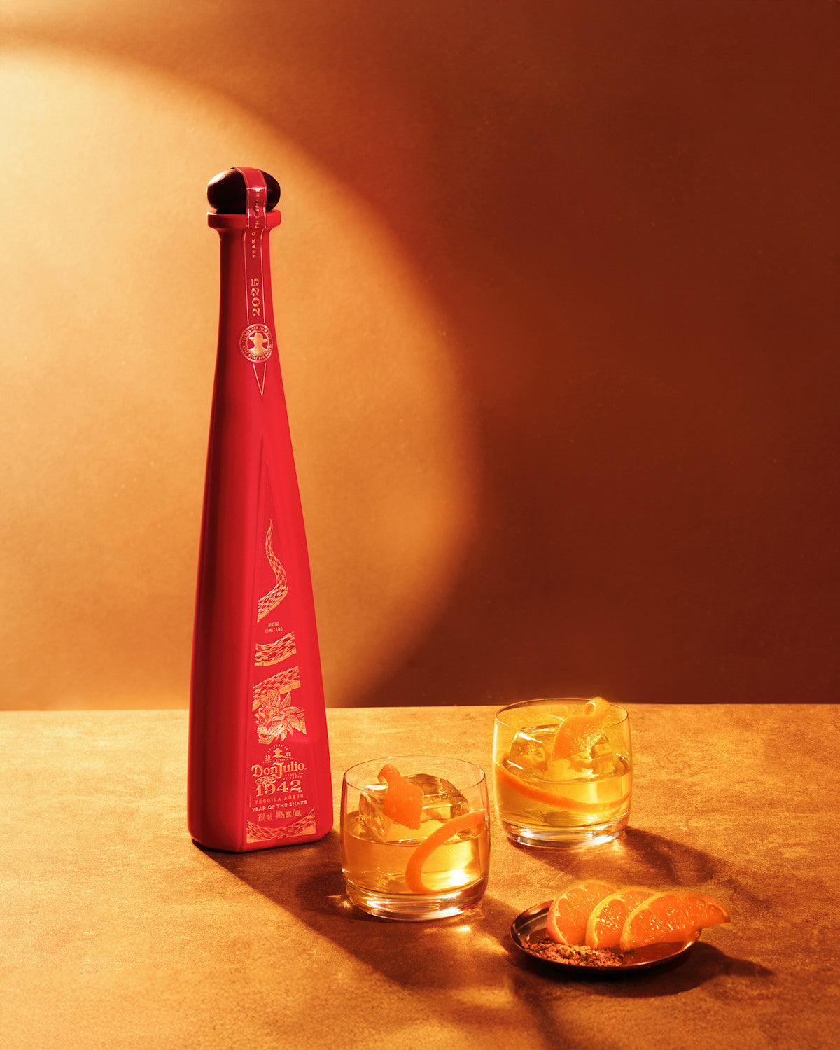 Don Julio 1942 Year of the Snake Añejo Tequila bottle with cocktails and orange garnish on a warm background.