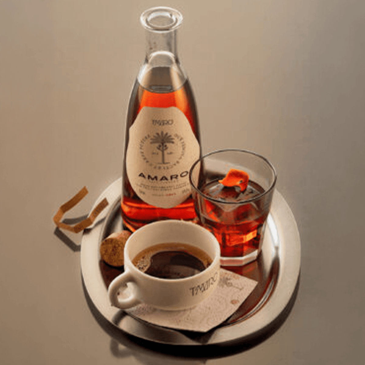 Bottle of T'maro Amaro 700ml on a tray with an iced drink and coffee cup, showcasing premium herbal liqueur.