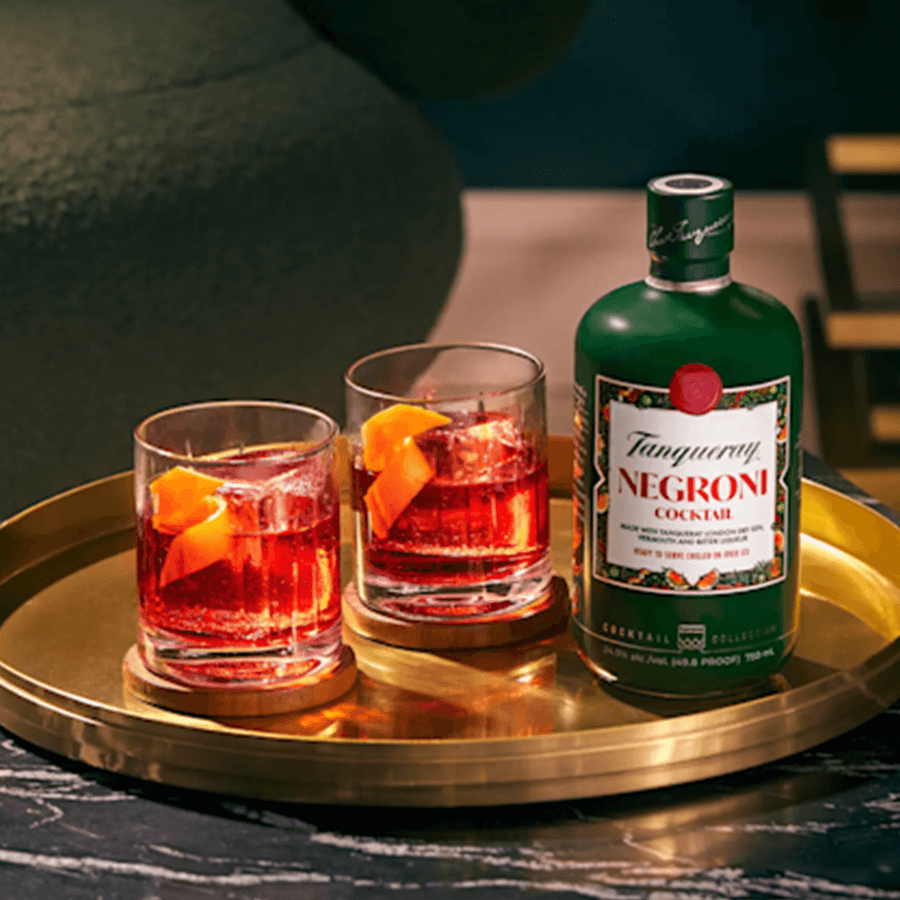 Tanqueray Negroni Cocktail 375ml displayed with two glasses on a golden tray, showcasing vibrant colors and garnished with orange.