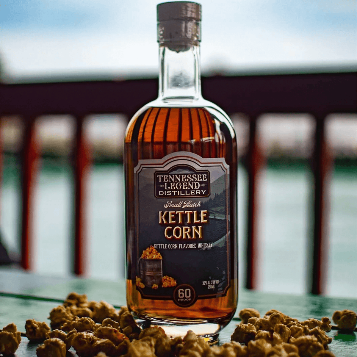 Tennessee Legend Kettle Corn Whiskey bottle with popcorn kernels on a wooden table, showcasing sweet and savory flavor.