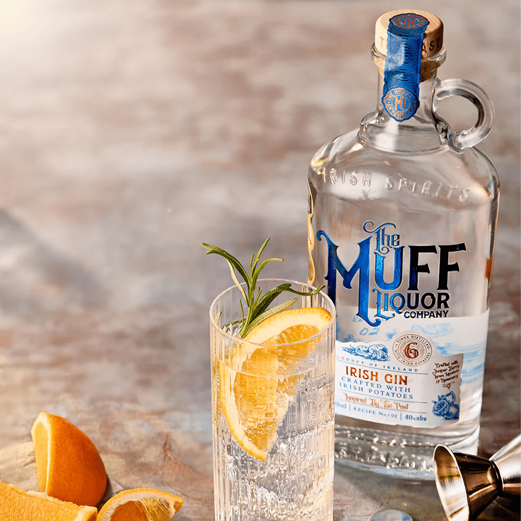 The Muff Liquor Irish Potato Gin 700ml bottle beside a refreshing gin cocktail garnished with orange and rosemary.