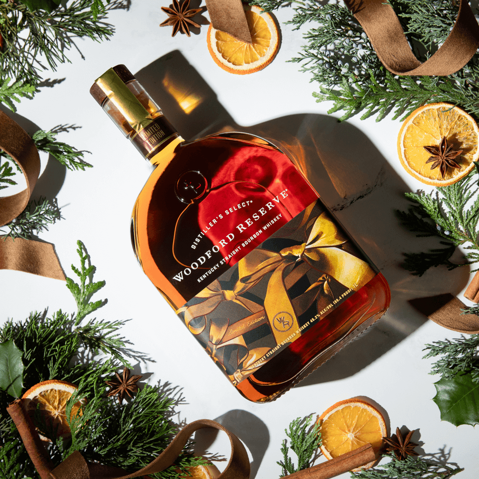 Woodford Reserve 2024 Holiday Edition bourbon bottle surrounded by festive decorations and greenery.