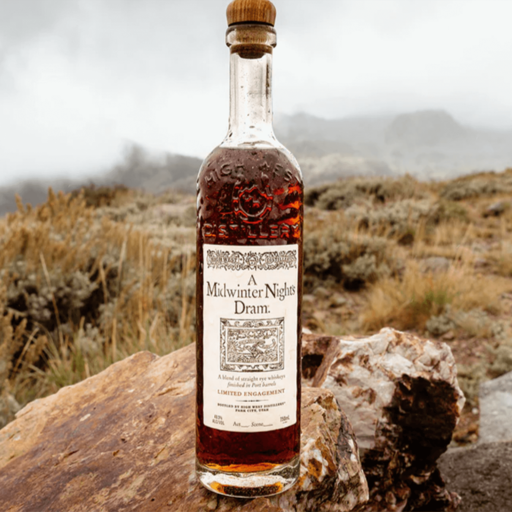 Bottle of High West A Midwinter Nights Dram whiskey on rocky terrain with a cloudy background.