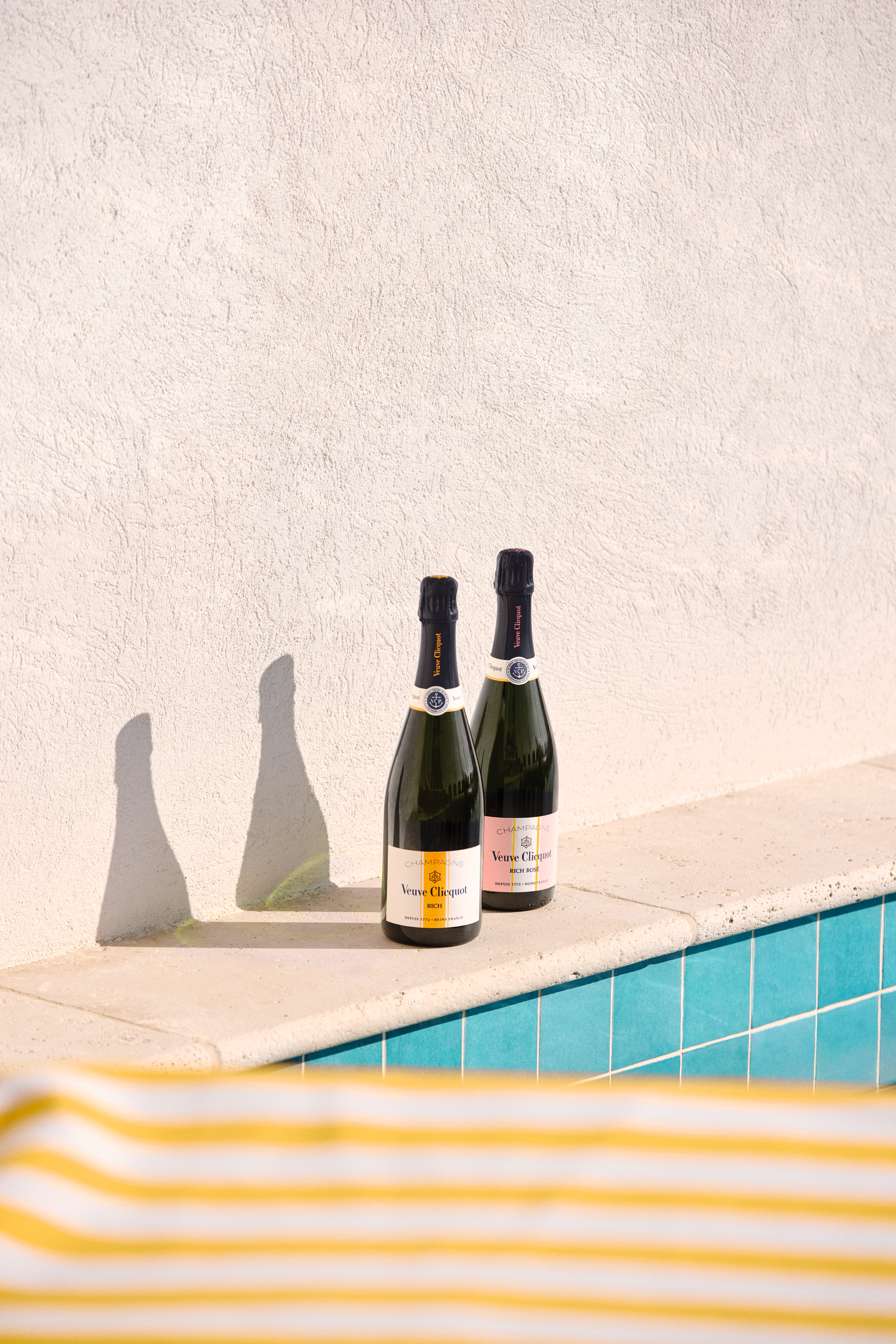 Two bottles of Veuve Clicquot RICH Champagne on a poolside ledge, perfect for summer gatherings.