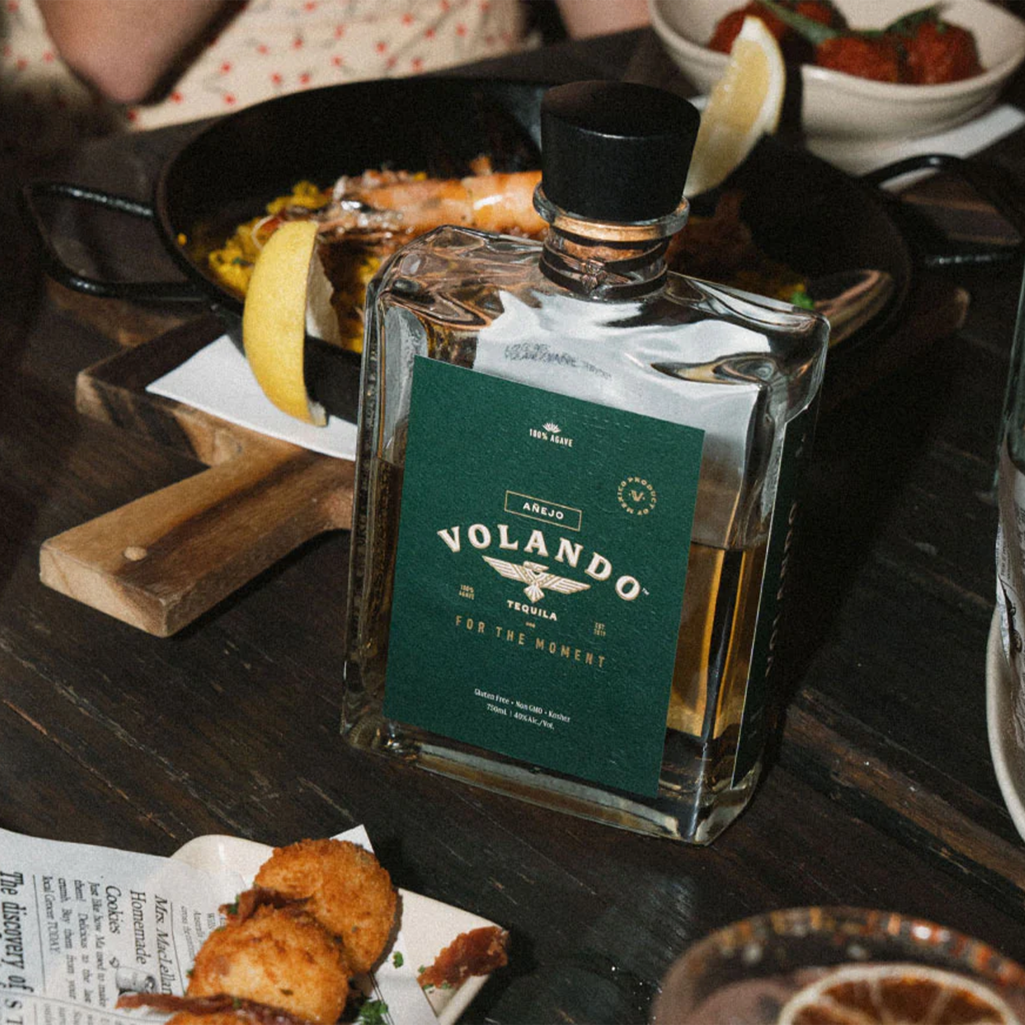 Bottle of Volando Añejo Tequila on a dining table with various dishes, highlighting its elegant design and rich flavors.