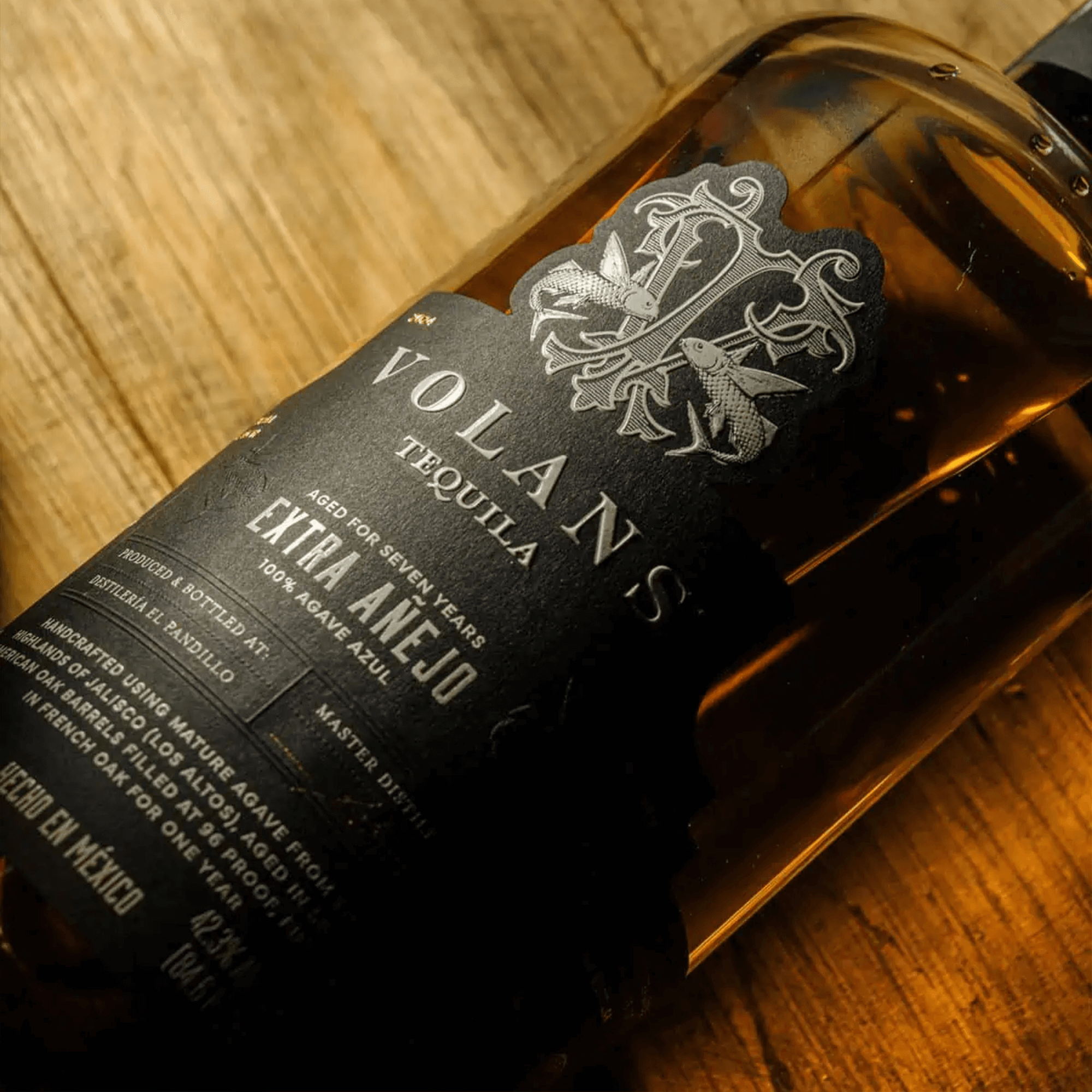 Bottle of Volans 7 Year Extra Añejo Tequila showcasing its elegant label and rich amber color on wooden background.