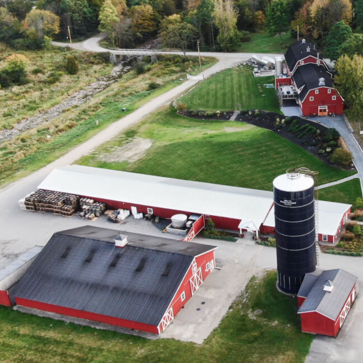 Aerial view of a red barn complex with a silo and surrounding green fields.