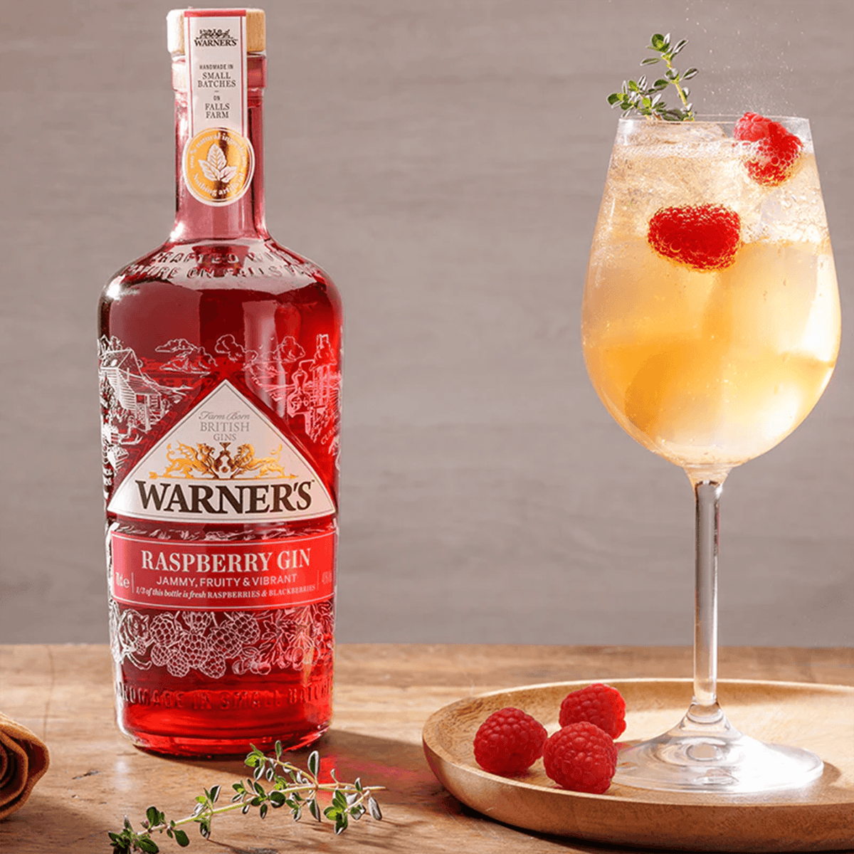 Bottle of Warner's Raspberry Gin with a refreshing cocktail and fresh raspberries, showcasing its fruity flavor.