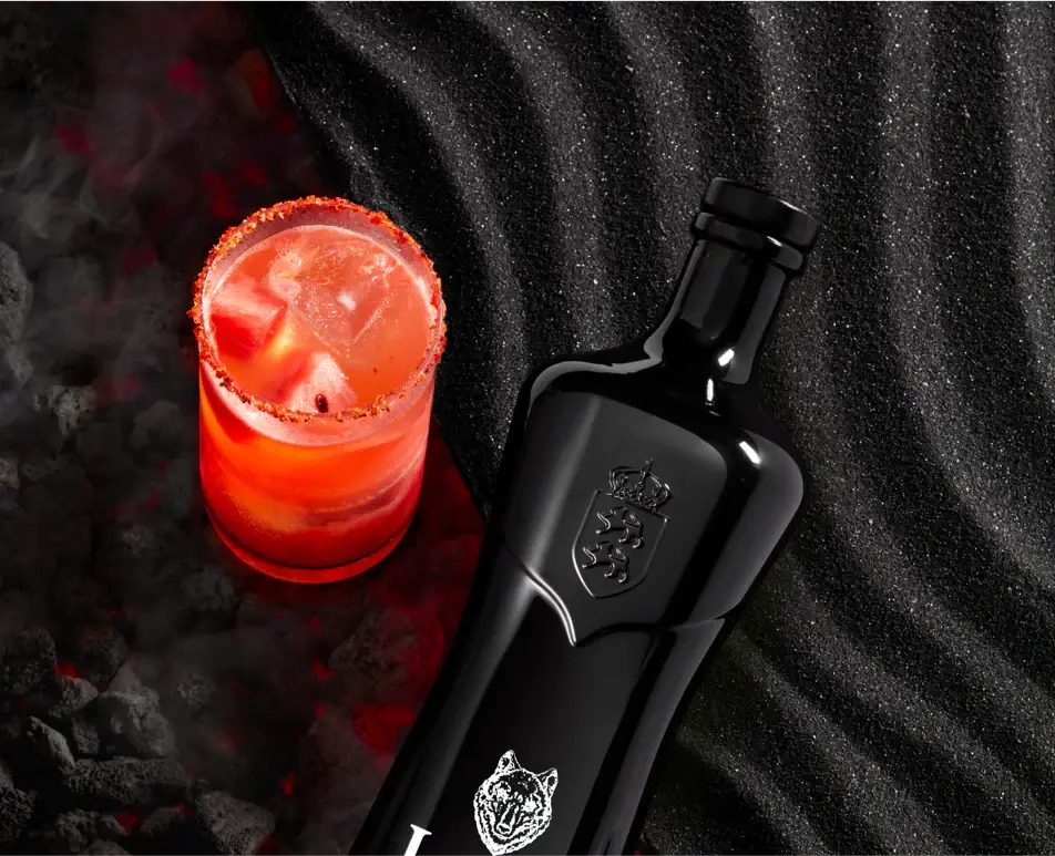 Lobos 1707 Artesanal Mezcal bottle beside a smoky cocktail on a textured black surface.
