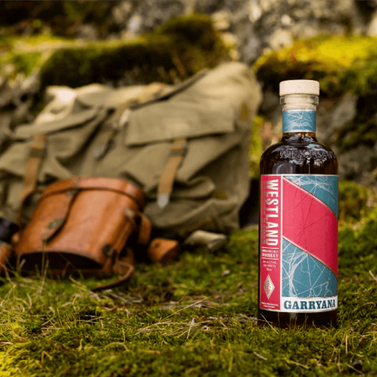 Westland Garryana 9th Edition 700ml bottle on mossy ground with a backpack, showcasing Pacific Northwest terroir.