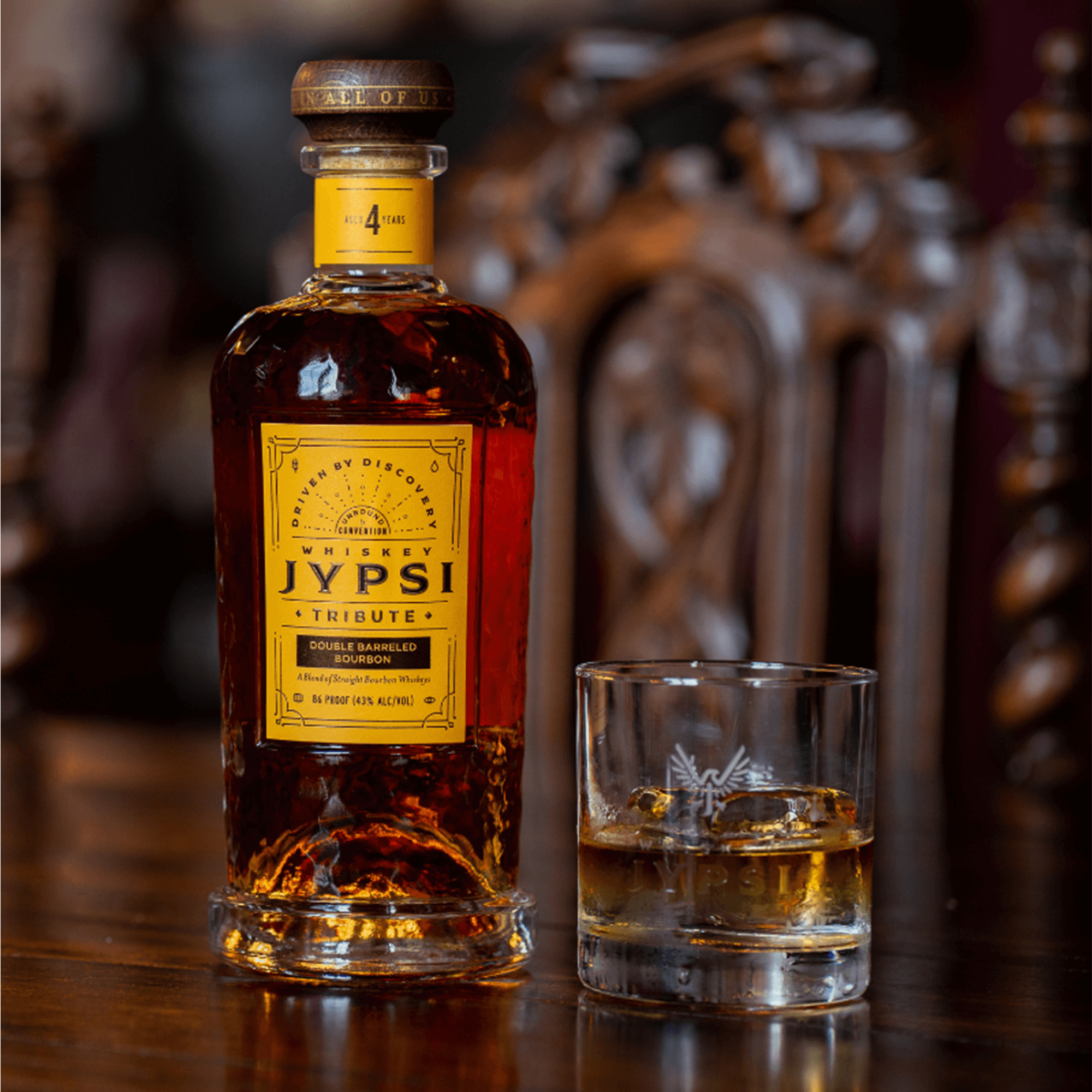Whiskey JYPSI Tribute Double Barreled Bourbon bottle with glass on wooden table.