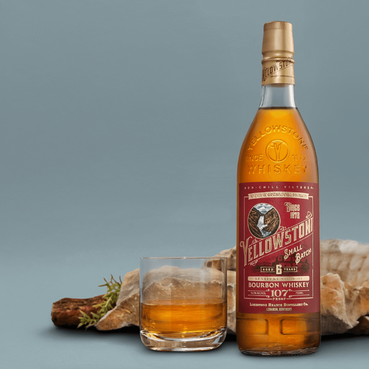 Yellowstone Small Batch 107 Bourbon Whiskey bottle with a glass on a rustic background.