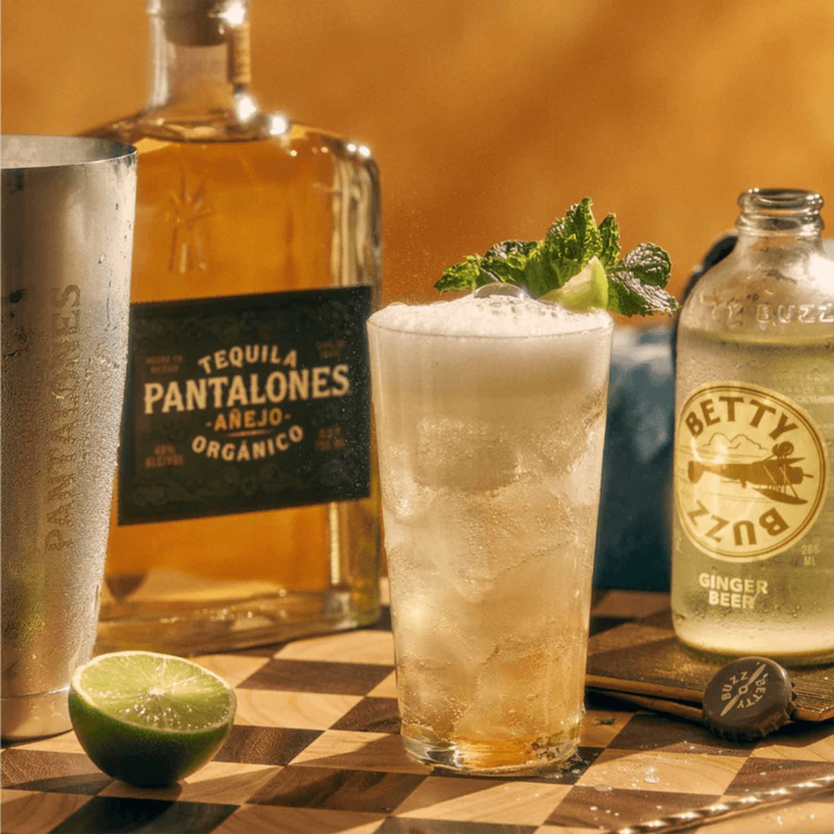 Refreshing Pantalones Añejo Tequila cocktail with ginger beer and lime, set against a warm backdrop.