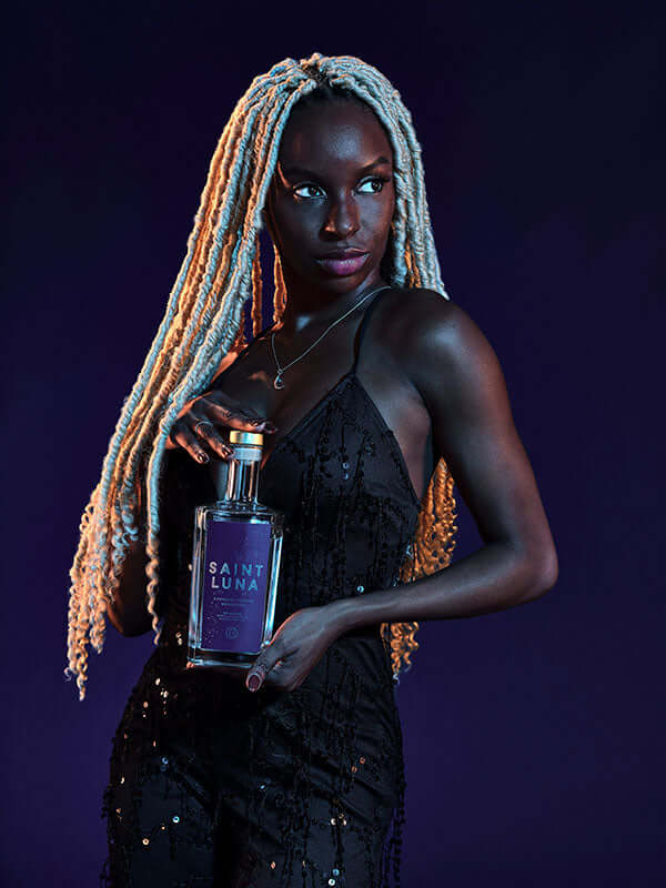 Model showcasing Saint Luna Charcoal Filtered Moonshine bottle against a dark, vibrant background.