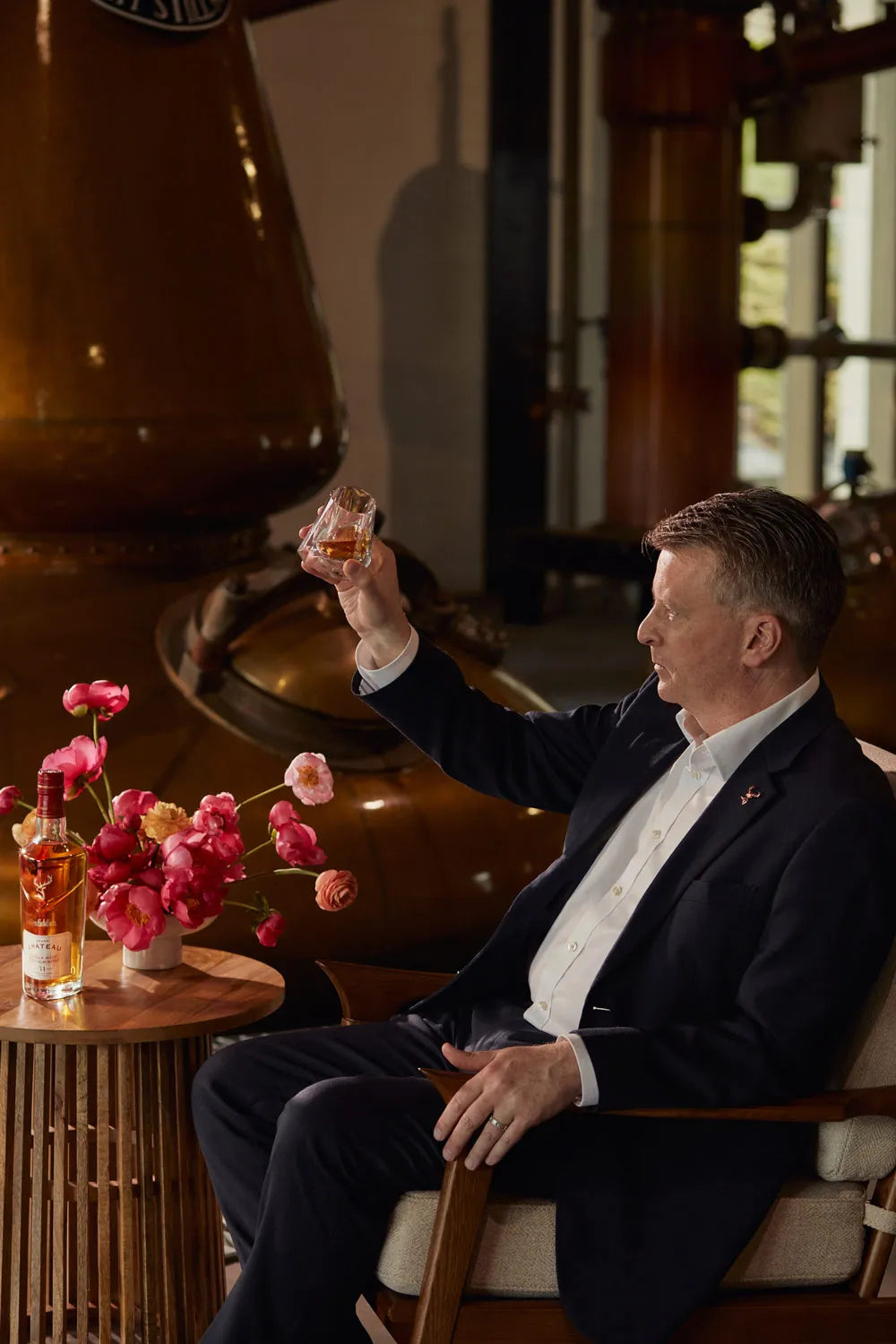 Man enjoying a glass of Glenfiddich Grand Château whisky in a distillery setting.