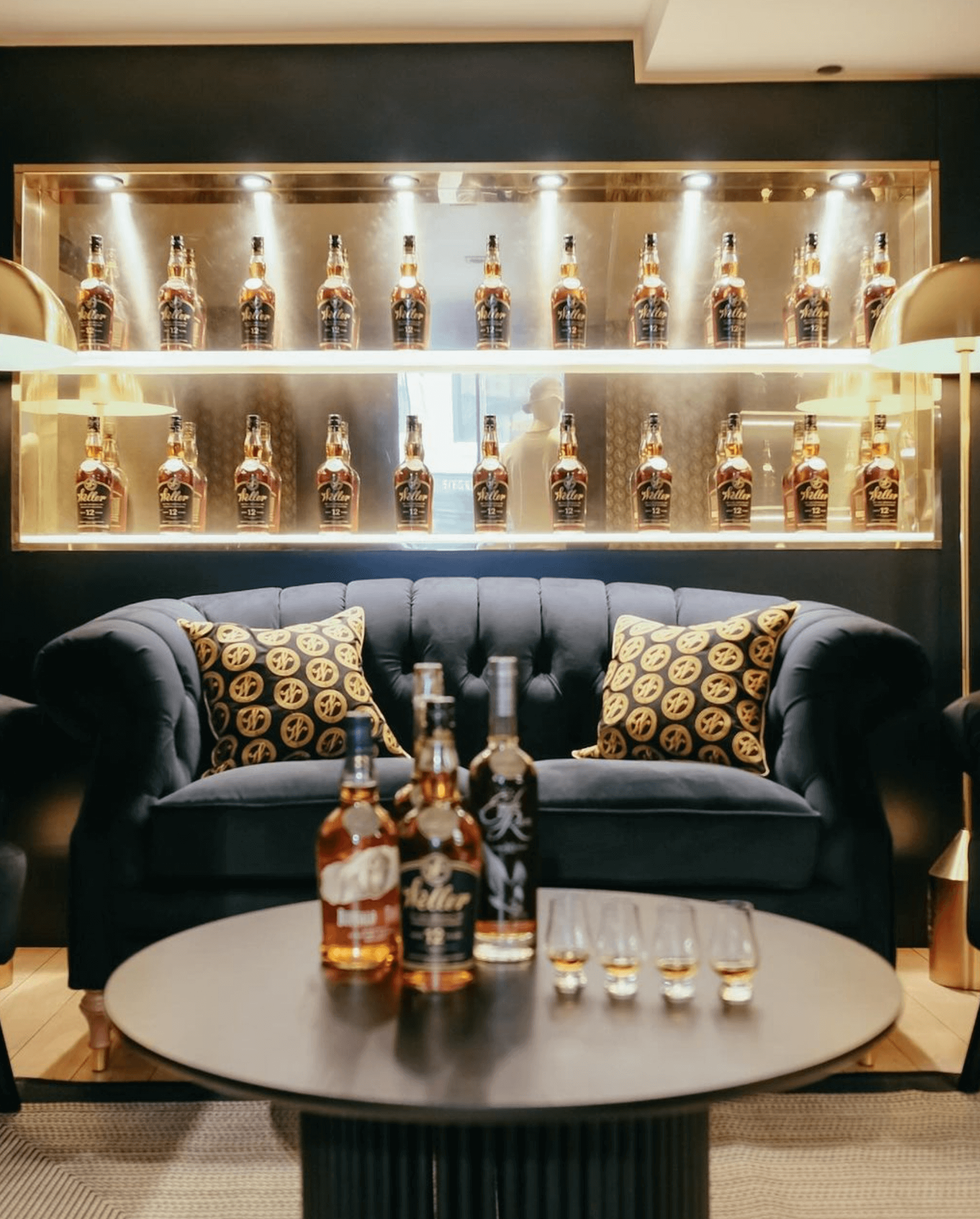 Stylish lounge showcasing bottles of Eagle Rare bourbon on display shelves, with a cozy sofa and tasting glasses.