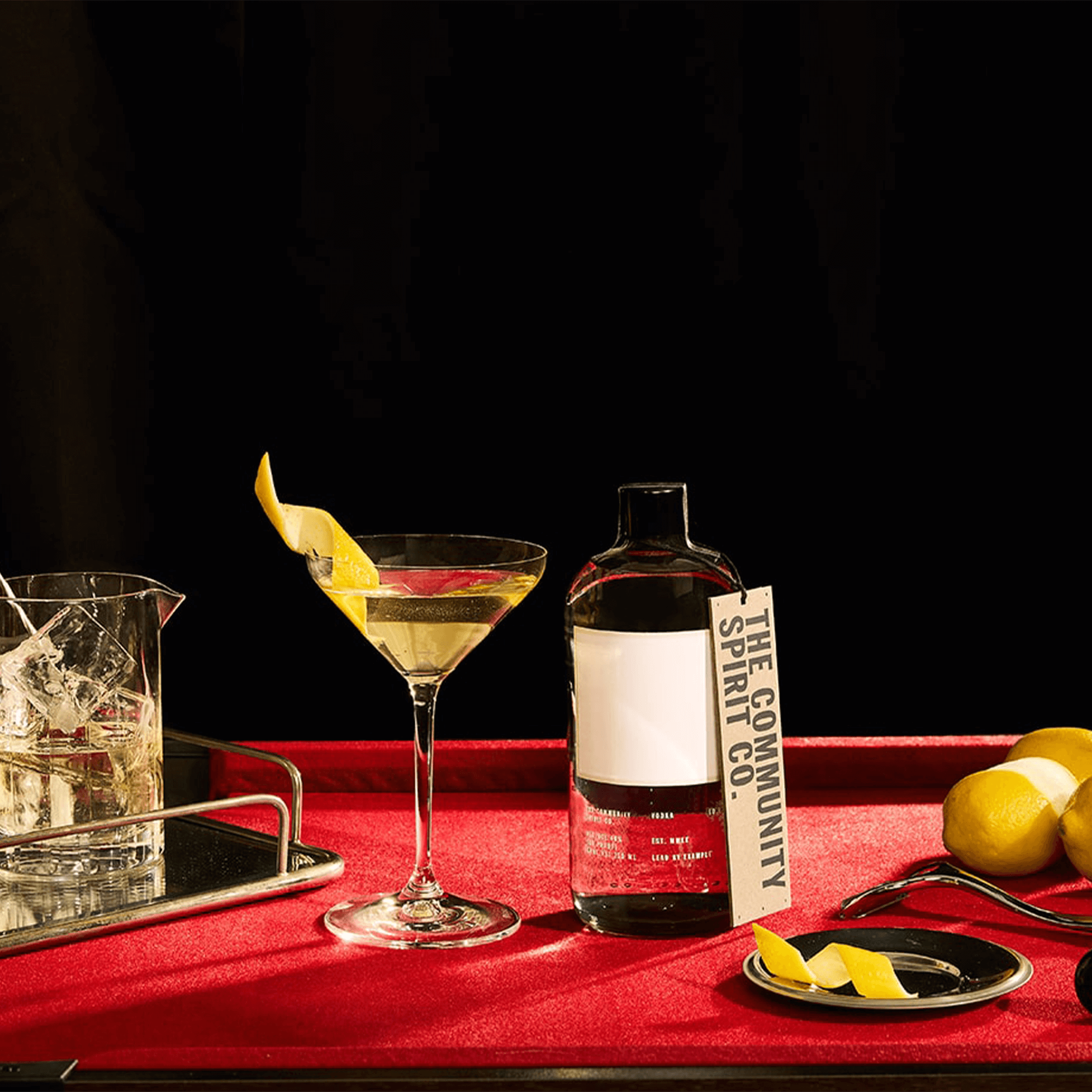 Community Spirit Vodka bottle with cocktail and lemon twist on a vibrant red table.
