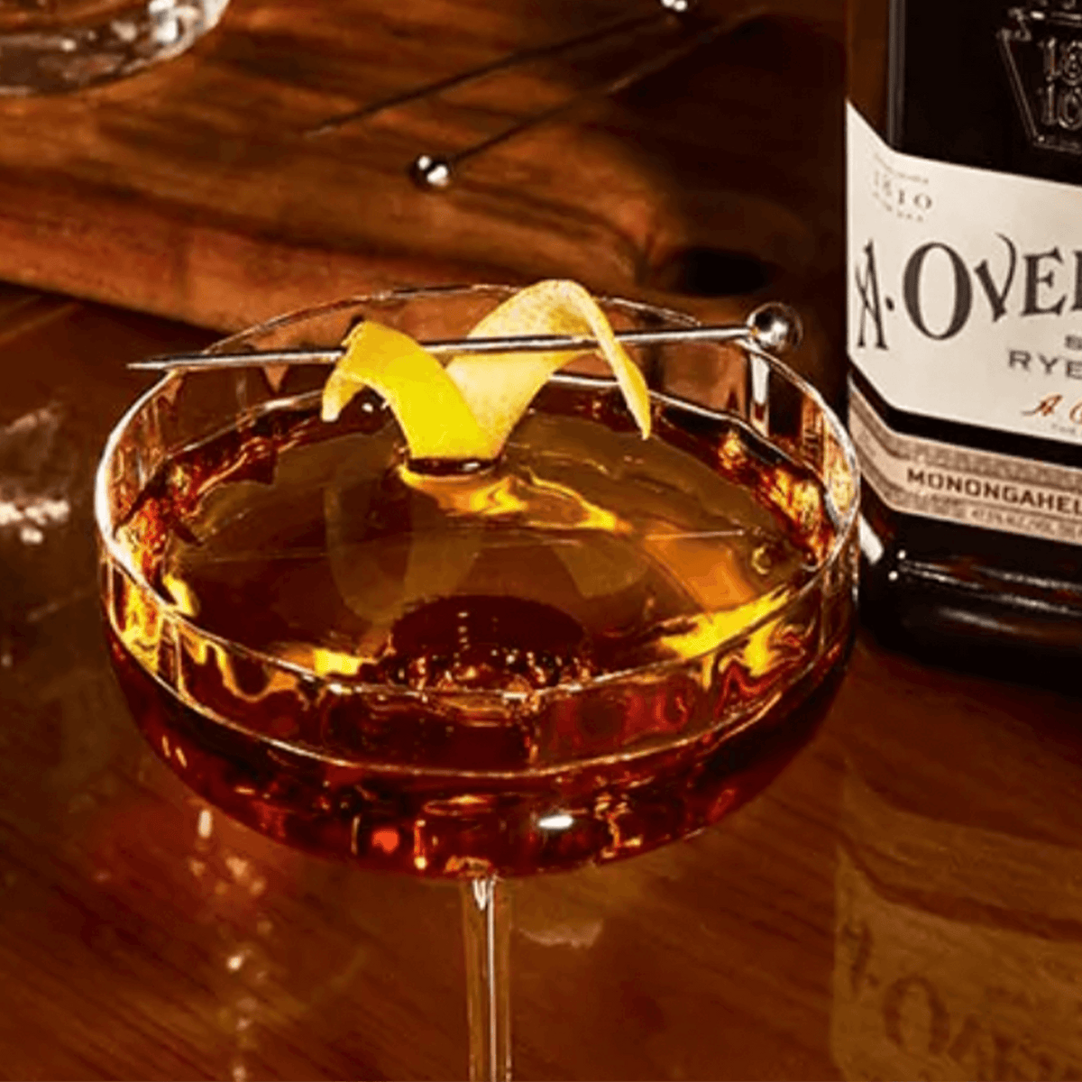 A cocktail made with A. Overholt 4 Year Rye Whiskey, garnished with lemon peel, on a wooden surface.