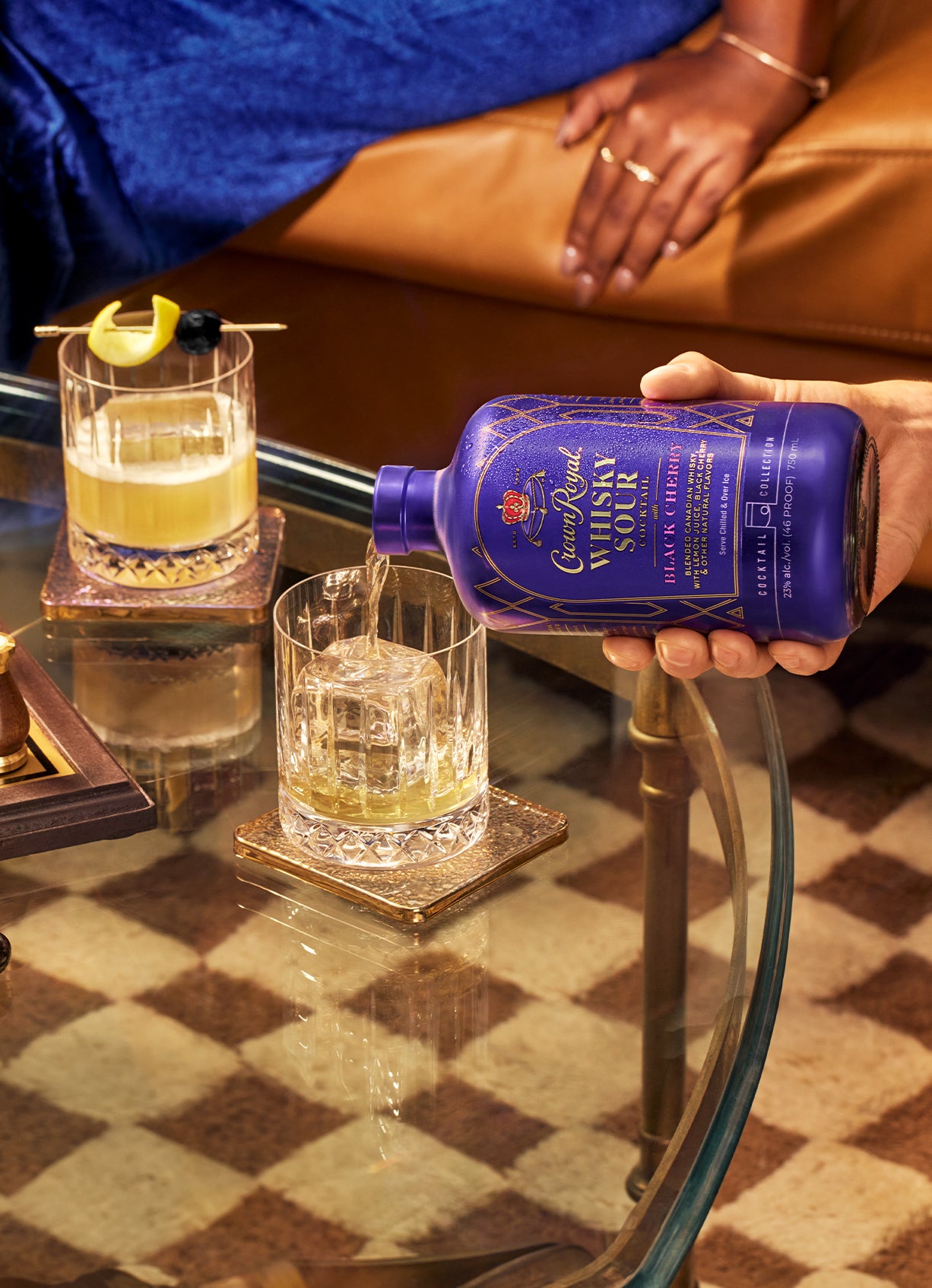Pouring Crown Royal Whisky Sour cocktail into a glass, with a stylish setup featuring drinks and casual setting.
