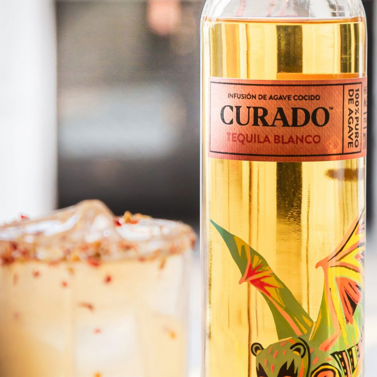 Curado Blue Agave Blanco Tequila bottle with floral decoration, showcasing 100% agave in a stylish setting.