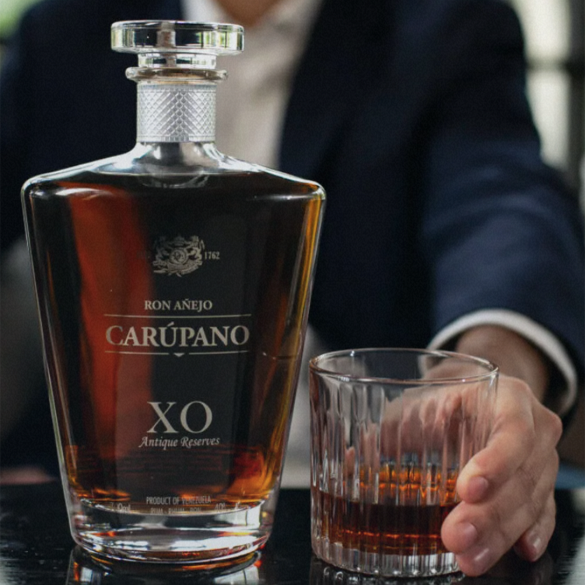 Ron Carupano Anejo XO Antique Reserve Rum bottle with a glass, showcasing its rich amber color and elegant packaging.