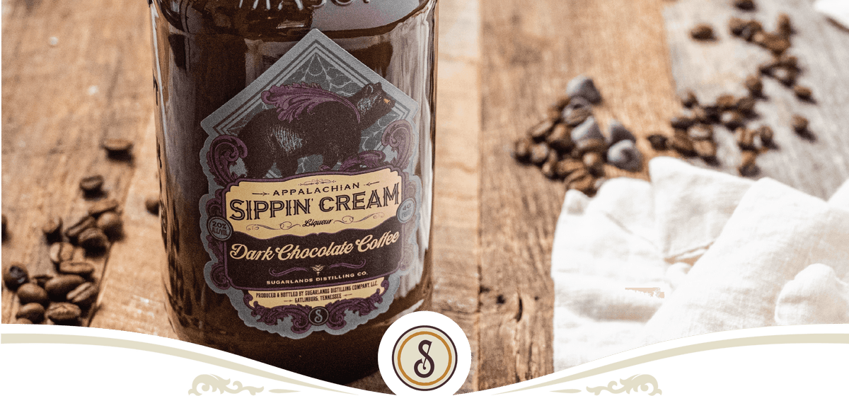 Dark Chocolate Coffee Sippin' Cream bottle surrounded by coffee beans on a wooden table.