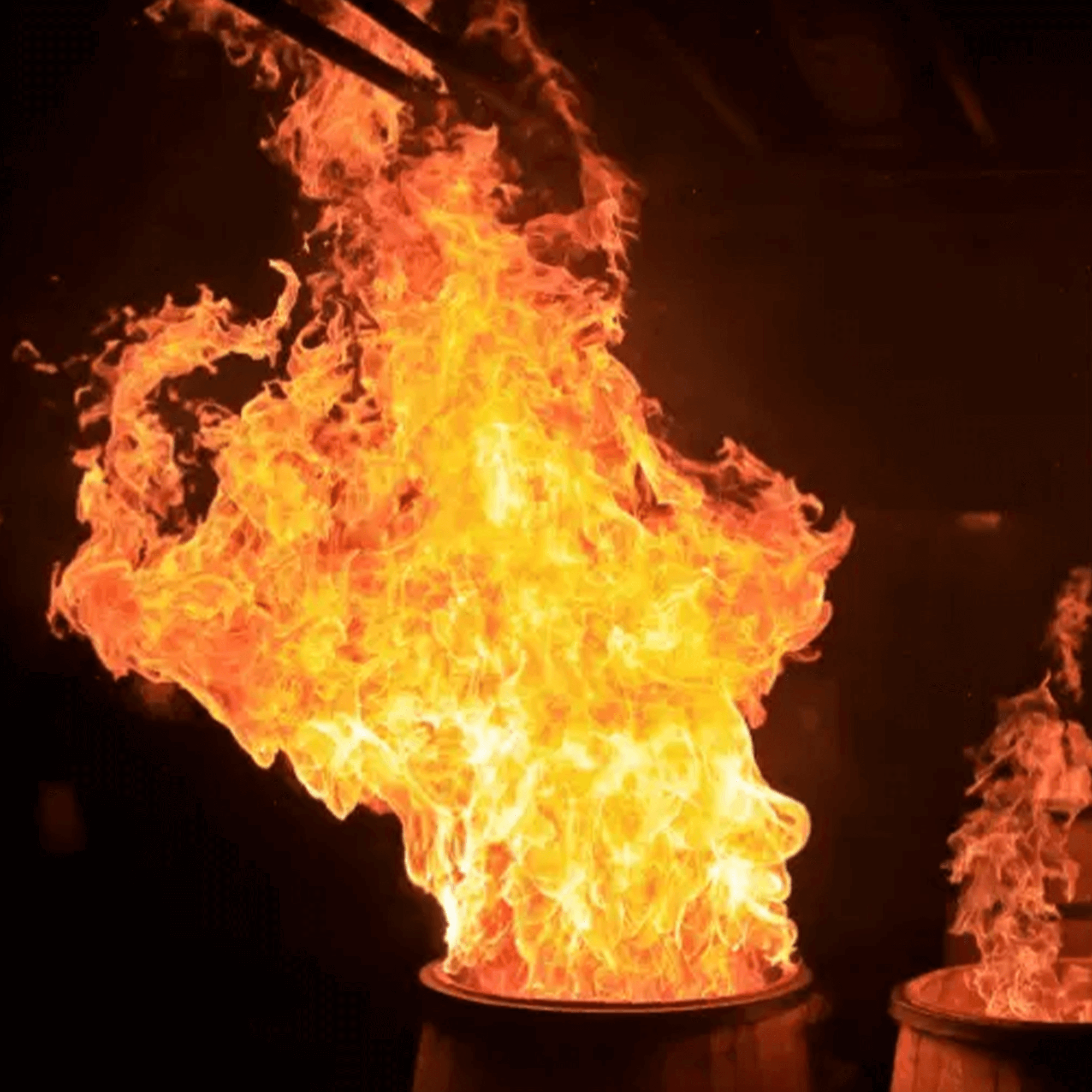 Flames rising dramatically from barrels, showcasing the fiery char process in bourbon aging.