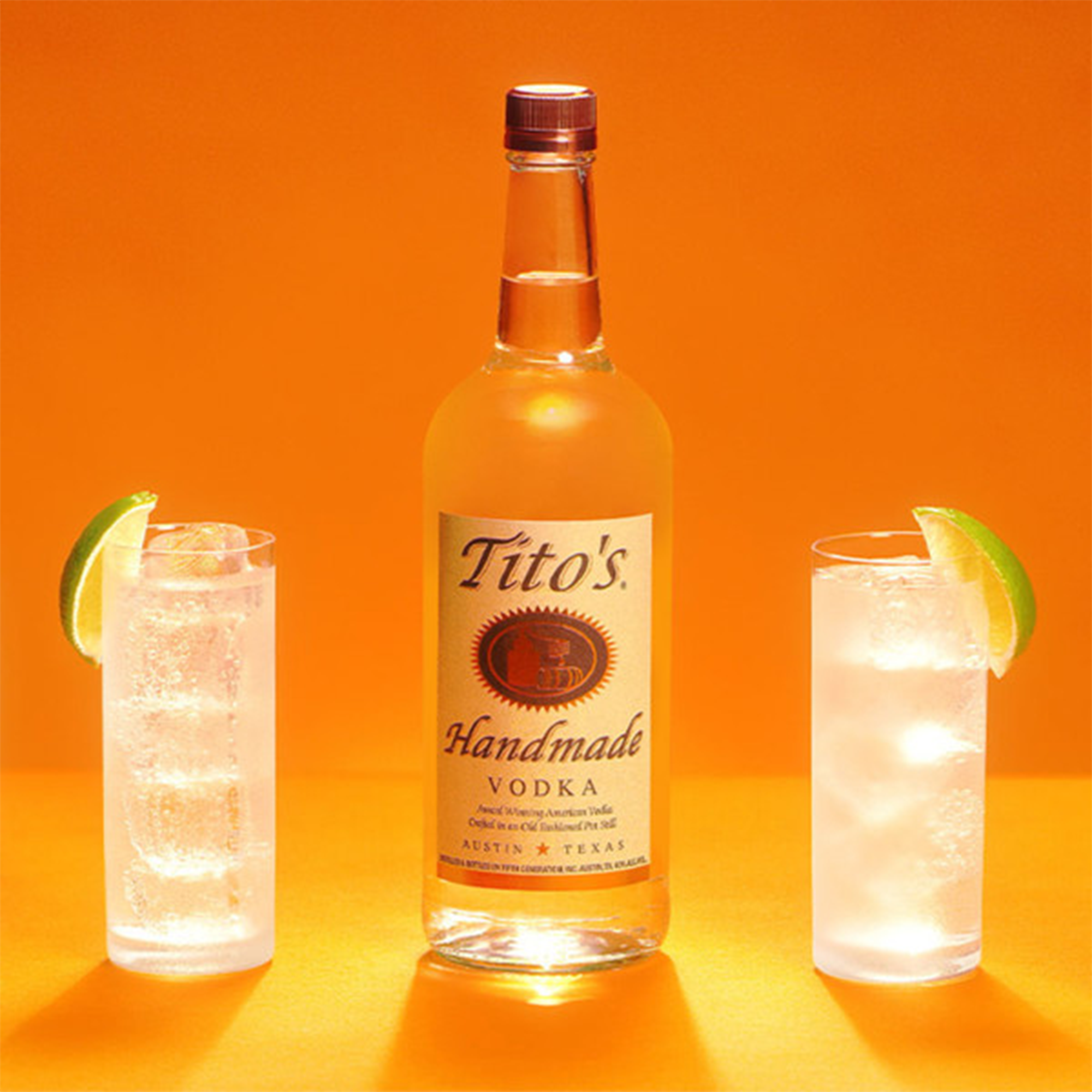 A bottle of Tito's Handmade Vodka with two refreshing cocktails on an orange background.
