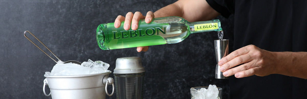 Pouring Leblon Cachaça from the bottle into a jigger, surrounded by ice and cocktail equipment.