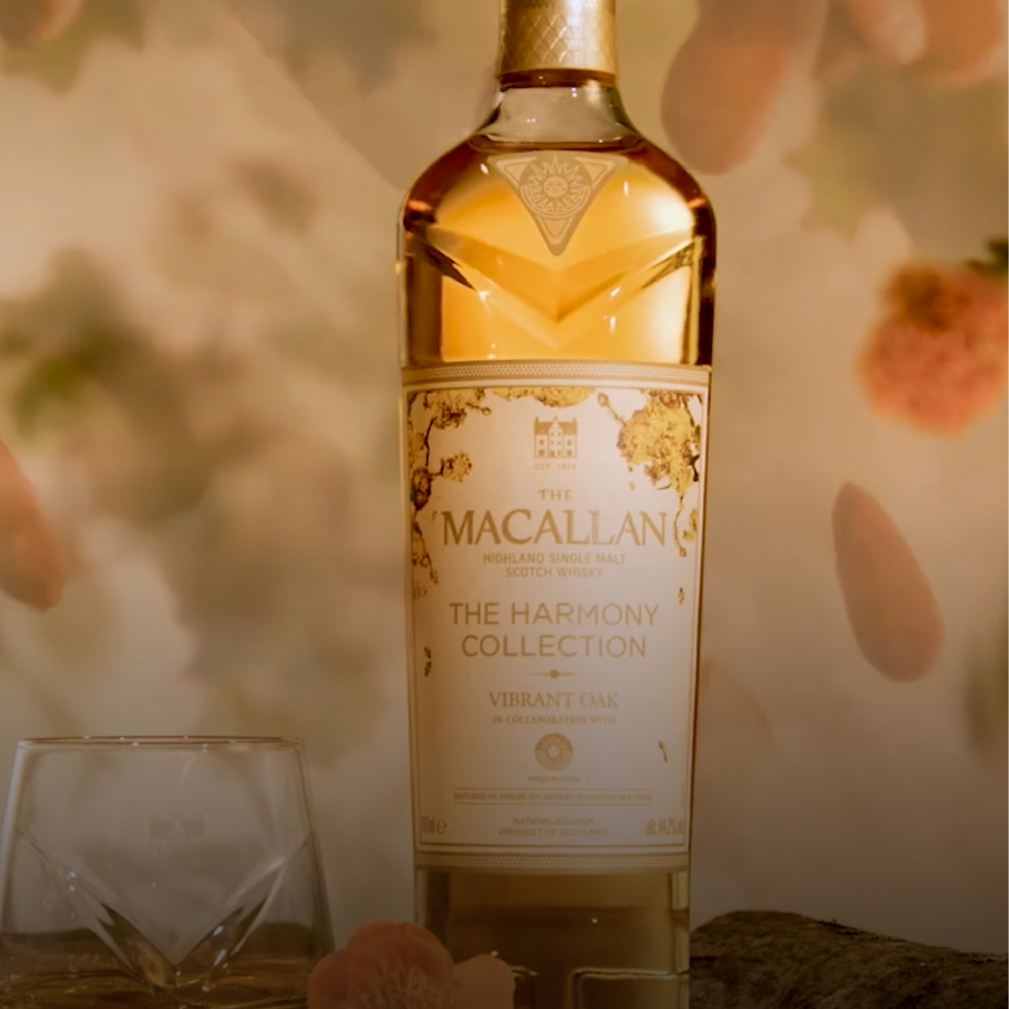 Macallan Harmony Collection Vibrant Oak Single Malt Scotch whisky bottle alongside glassware on a stylish backdrop.
