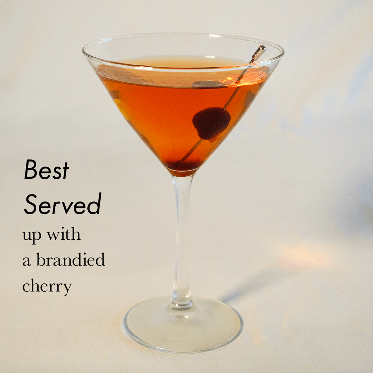 Freitag Manhattan cocktail in a martini glass garnished with a brandied cherry, showcasing a rich amber color.