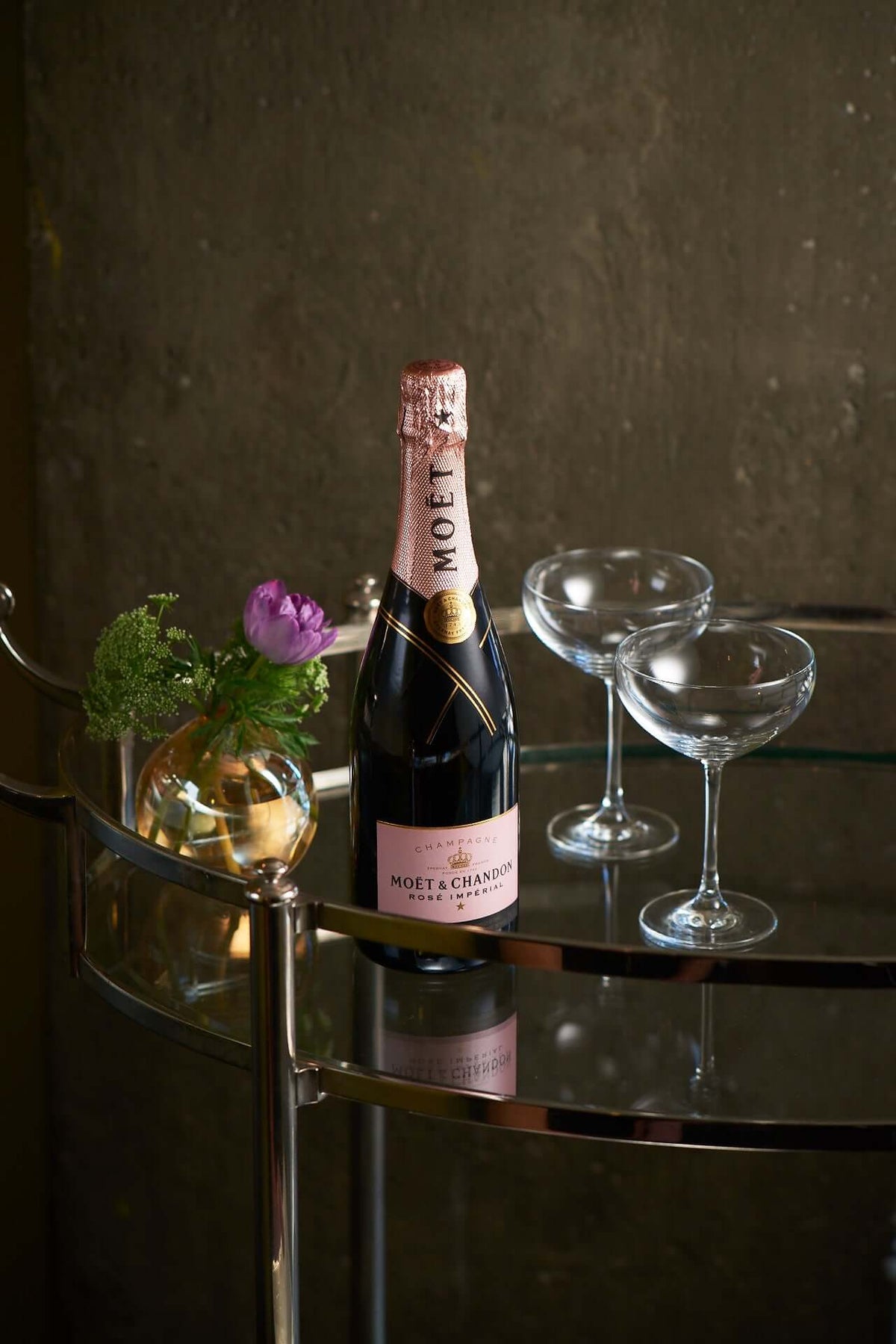 Bottle of Moët & Chandon Rosé Impérial on a bar cart with two champagne glasses and a floral accent.