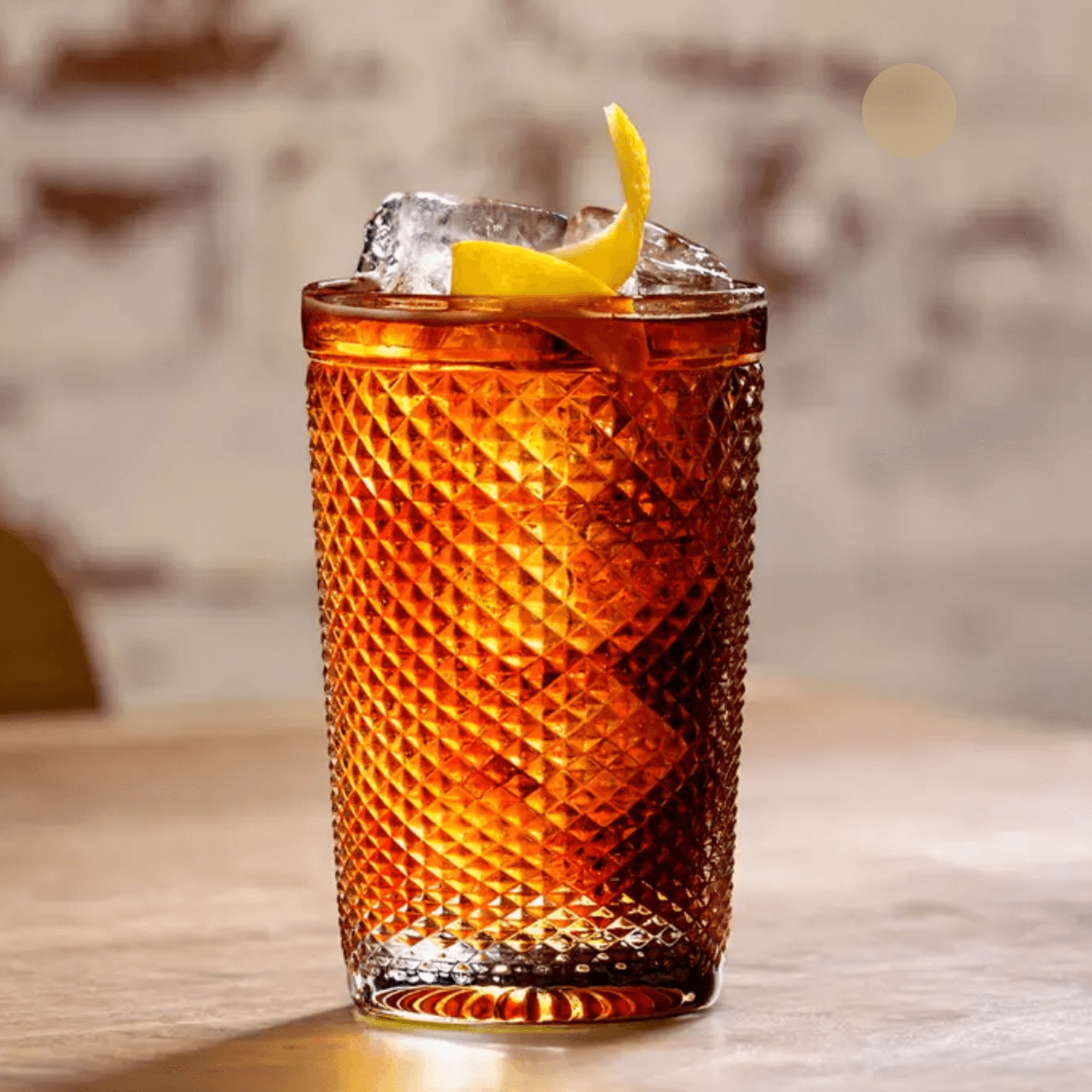 A beautifully crafted cocktail with a hint of yellow lemon garnish in a textured glass.